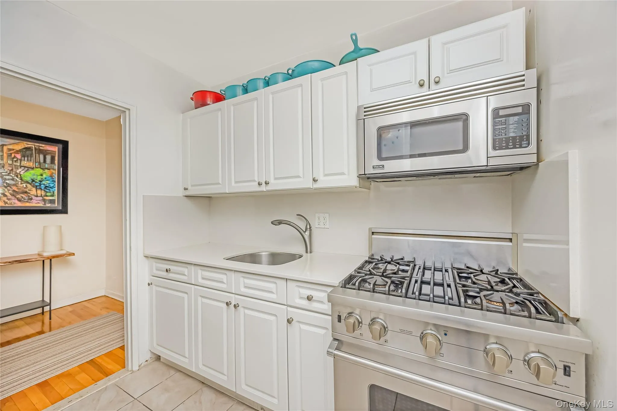 Kitchen featuring white cabinetry, light-toned countertops, a stainless steel range with gas burners, a stainless steel over-the-range microwave, and a stainless steel sink with a gooseneck faucet Kitchen featuring white cabinetry, light-toned countertops, a stainless steel range with gas burners, a stainless steel over-the-range microwave, and a stainless steel sink with a gooseneck faucet
