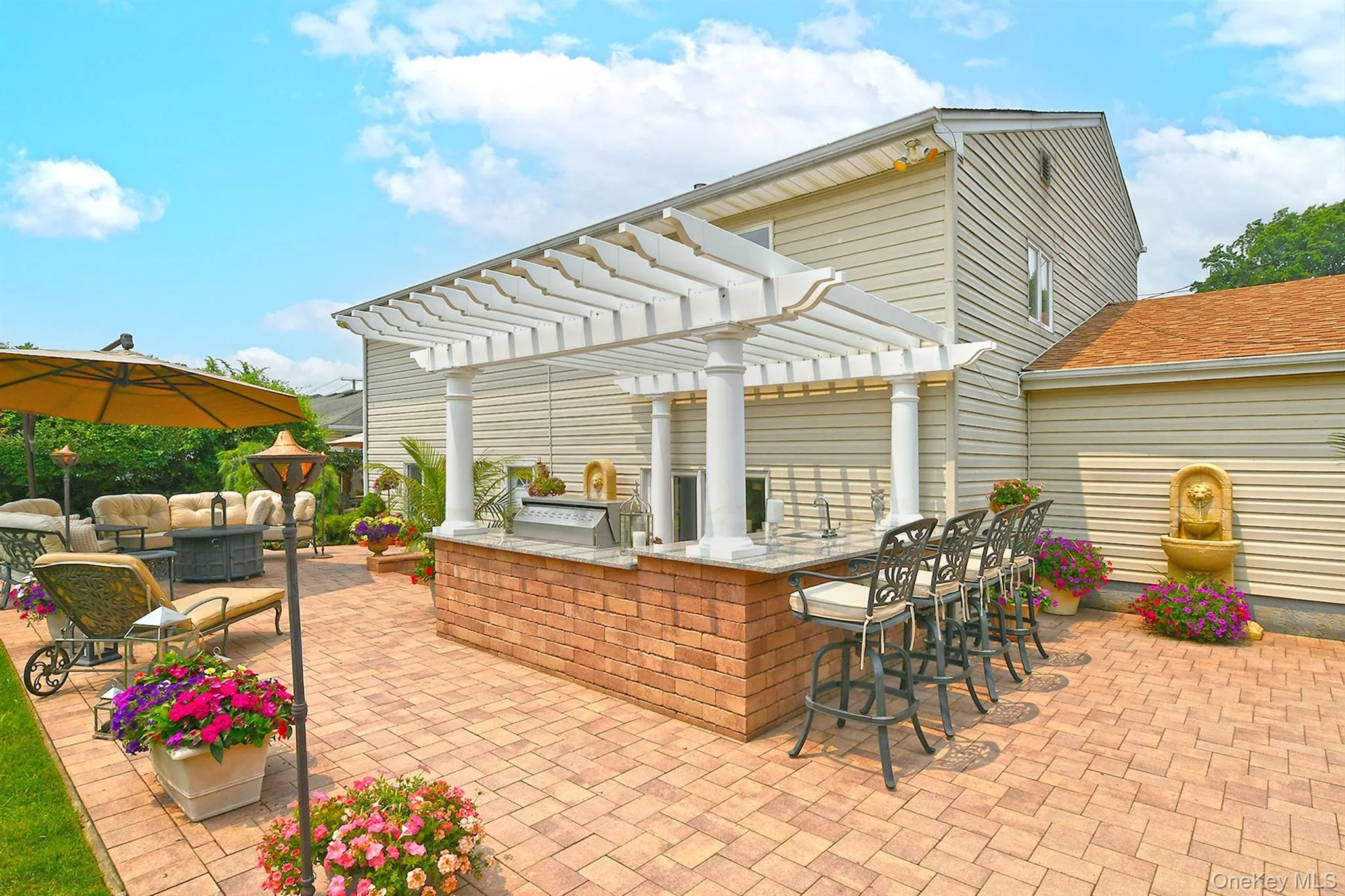 Spacious patio featuring a brick paver surface, a built-in outdoor kitchen with a pergola, stone countertop, integrated grill, and a bar seating area Spacious patio featuring a brick paver surface, a built-in outdoor kitchen with a pergola, stone countertop, integrated grill, and a bar seating area