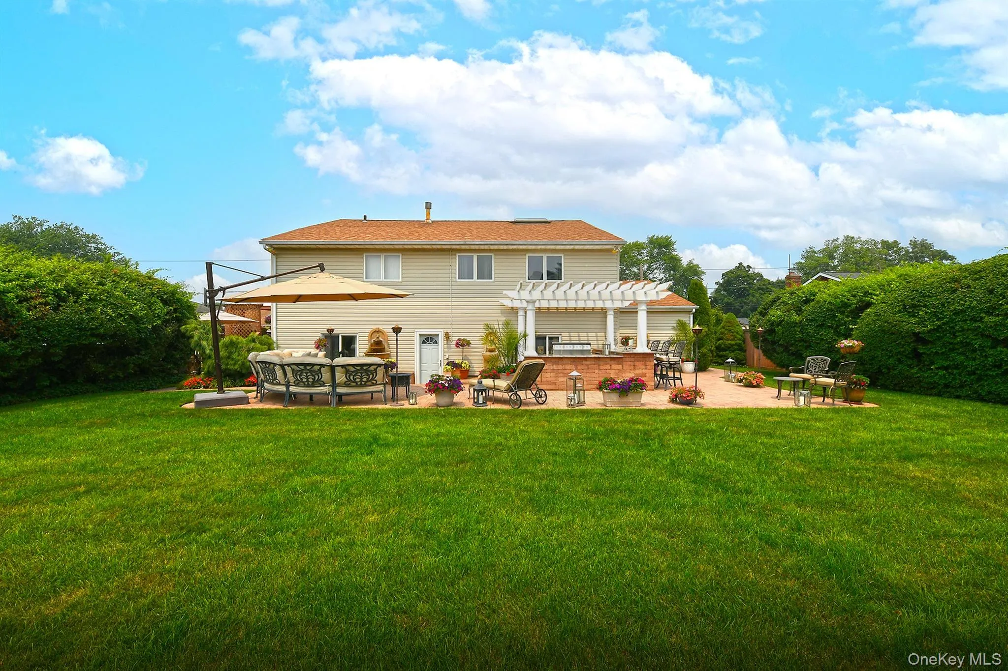 Expansive backyard featuring a manicured lawn, a large paver patio, a pergola-covered outdoor kitchen, and mature privacy landscaping Expansive backyard featuring a manicured lawn, a large paver patio, a pergola-covered outdoor kitchen, and mature privacy landscaping
