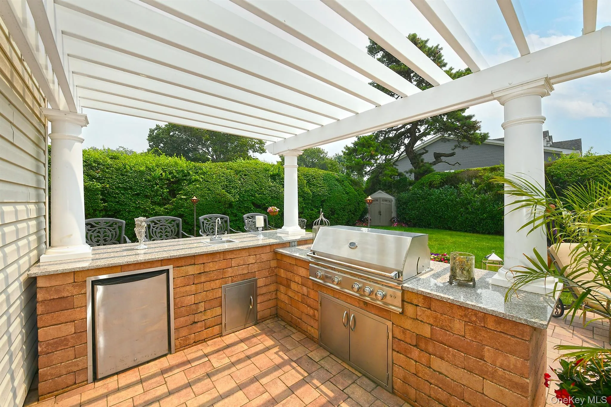 Outdoor kitchen featuring a built-in stainless steel grill, integrated refrigerator, granite countertops, and brick base Outdoor kitchen featuring a built-in stainless steel grill, integrated refrigerator, granite countertops, and brick base