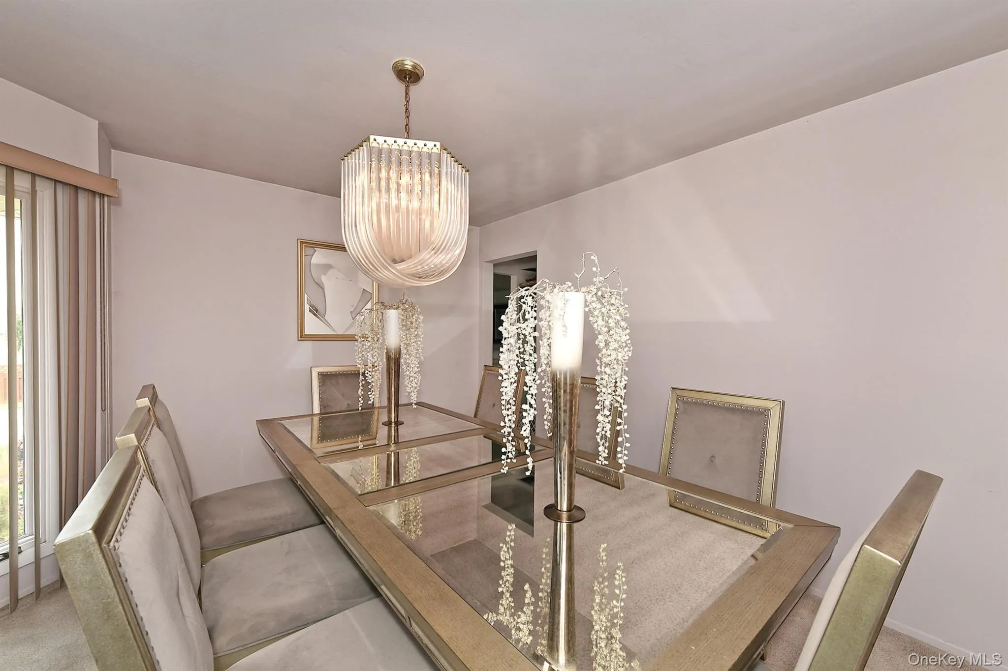 Dining area with a sophisticated pendant light fixture featuring fluted glass, neutral wall paint, and a large window with vertical blinds Dining area with a sophisticated pendant light fixture featuring fluted glass, neutral wall paint, and a large window with vertical blinds