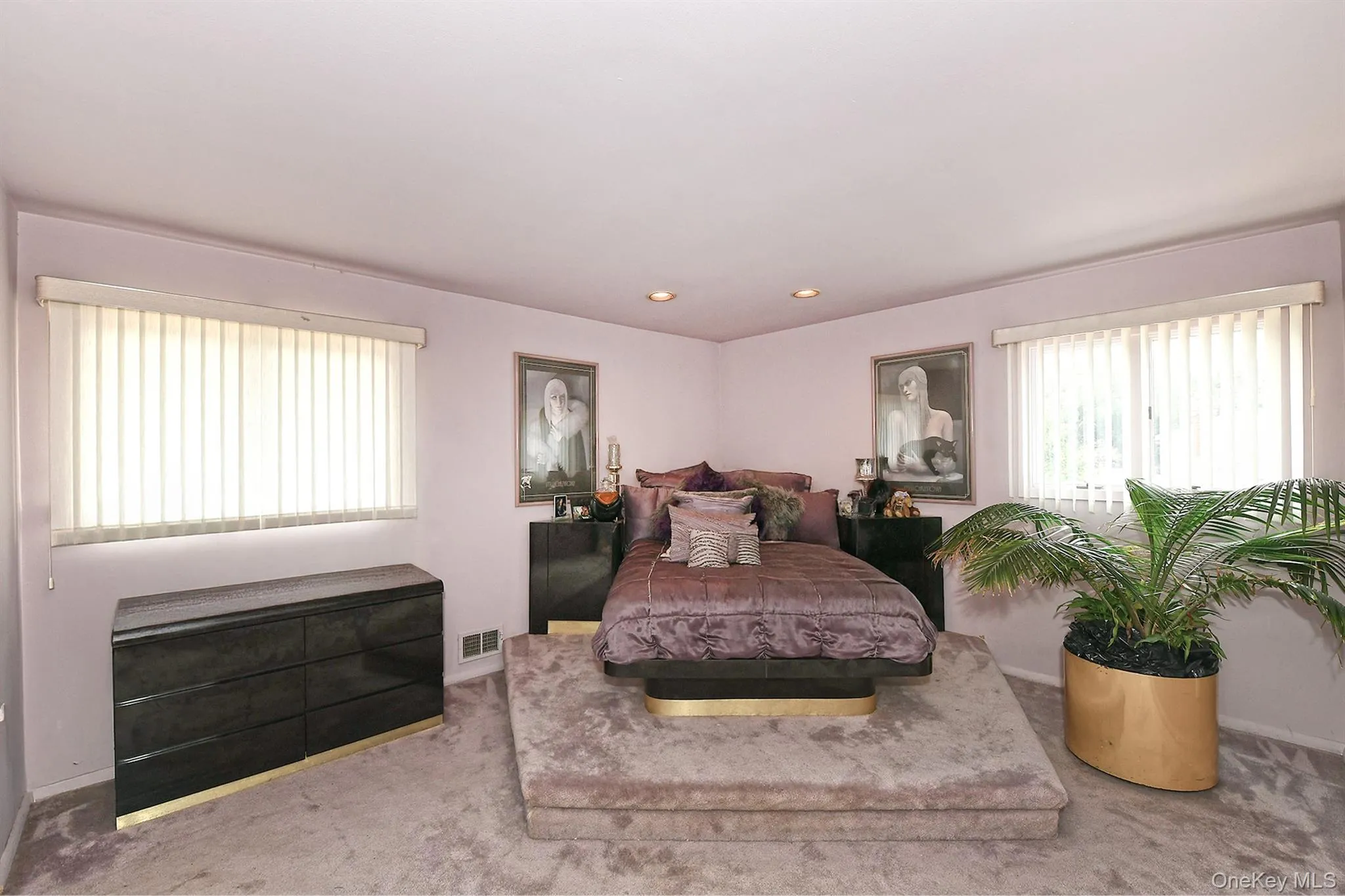 Carpeted bedroom featuring a raised platform for the bed, recessed lighting, and two windows with vertical blinds Carpeted bedroom featuring a raised platform for the bed, recessed lighting, and two windows with vertical blinds