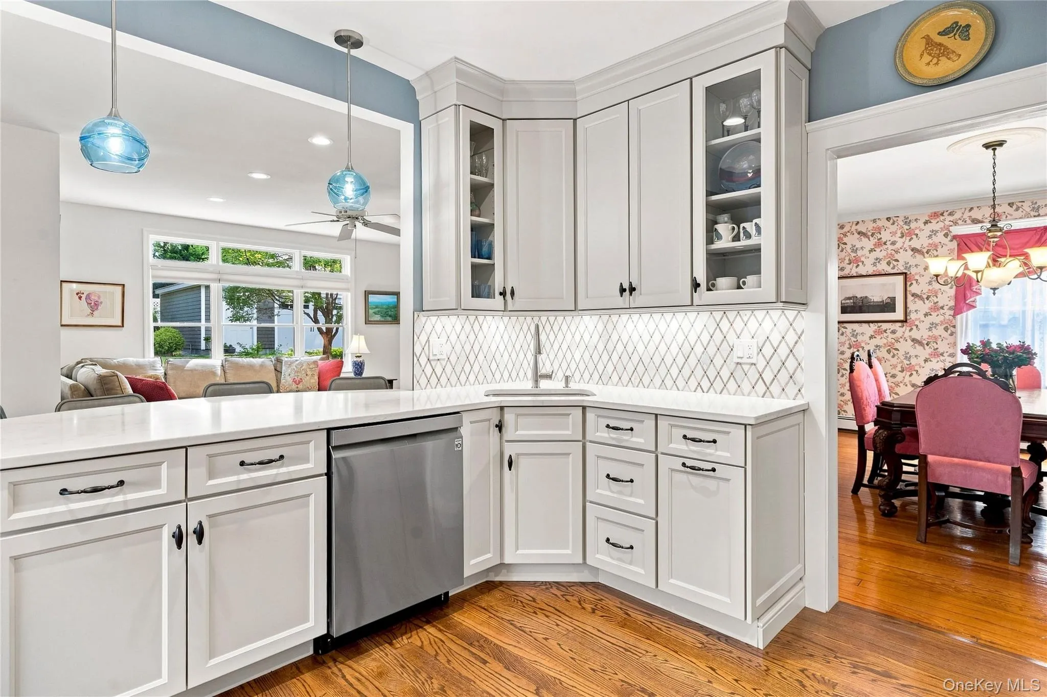 Kitchen with white cabinetry, quartz countertops, stainless steel dishwasher, diagonal tile backsplash, and wood-finish flooring Kitchen with white cabinetry, quartz countertops, stainless steel dishwasher, diagonal tile backsplash, and wood-finish flooring