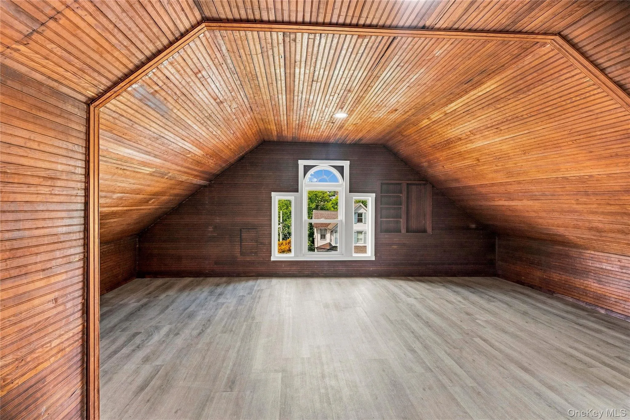 Attic space featuring wood-paneled walls and ceiling, a built-in window arch, light-toned wood-finish flooring, and recessed lighting Attic space featuring wood-paneled walls and ceiling, a built-in window arch, light-toned wood-finish flooring, and recessed lighting