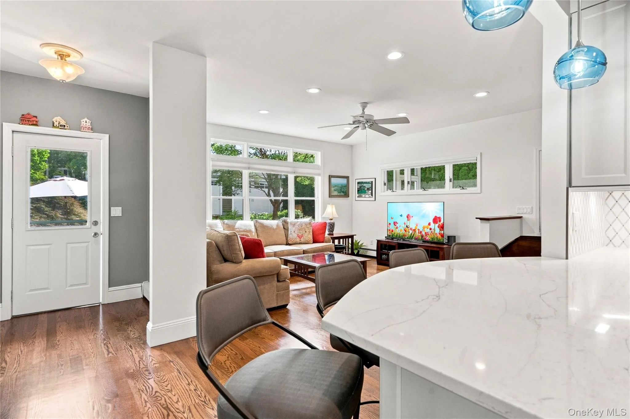 Hardwood flooring throughout, a ceiling fan with light fixture, and an open-concept design to a kitchen featuring a breakfast bar with pendant lighting Hardwood flooring throughout, a ceiling fan with light fixture, and an open-concept design to a kitchen featuring a breakfast bar with pendant lighting