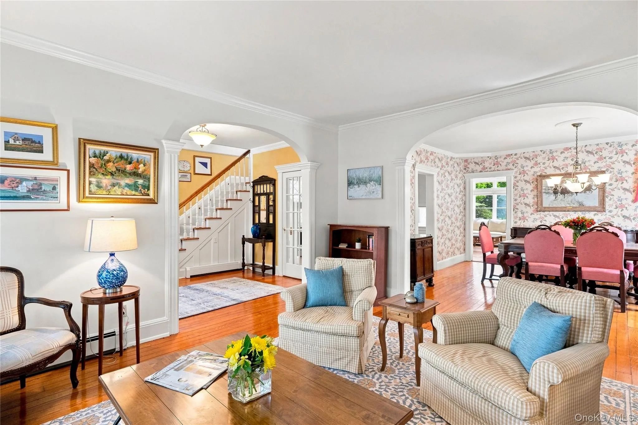 Hardwood flooring throughout, crown molding, arched doorways, and a staircase with white risers and handrail Hardwood flooring throughout, crown molding, arched doorways, and a staircase with white risers and handrail