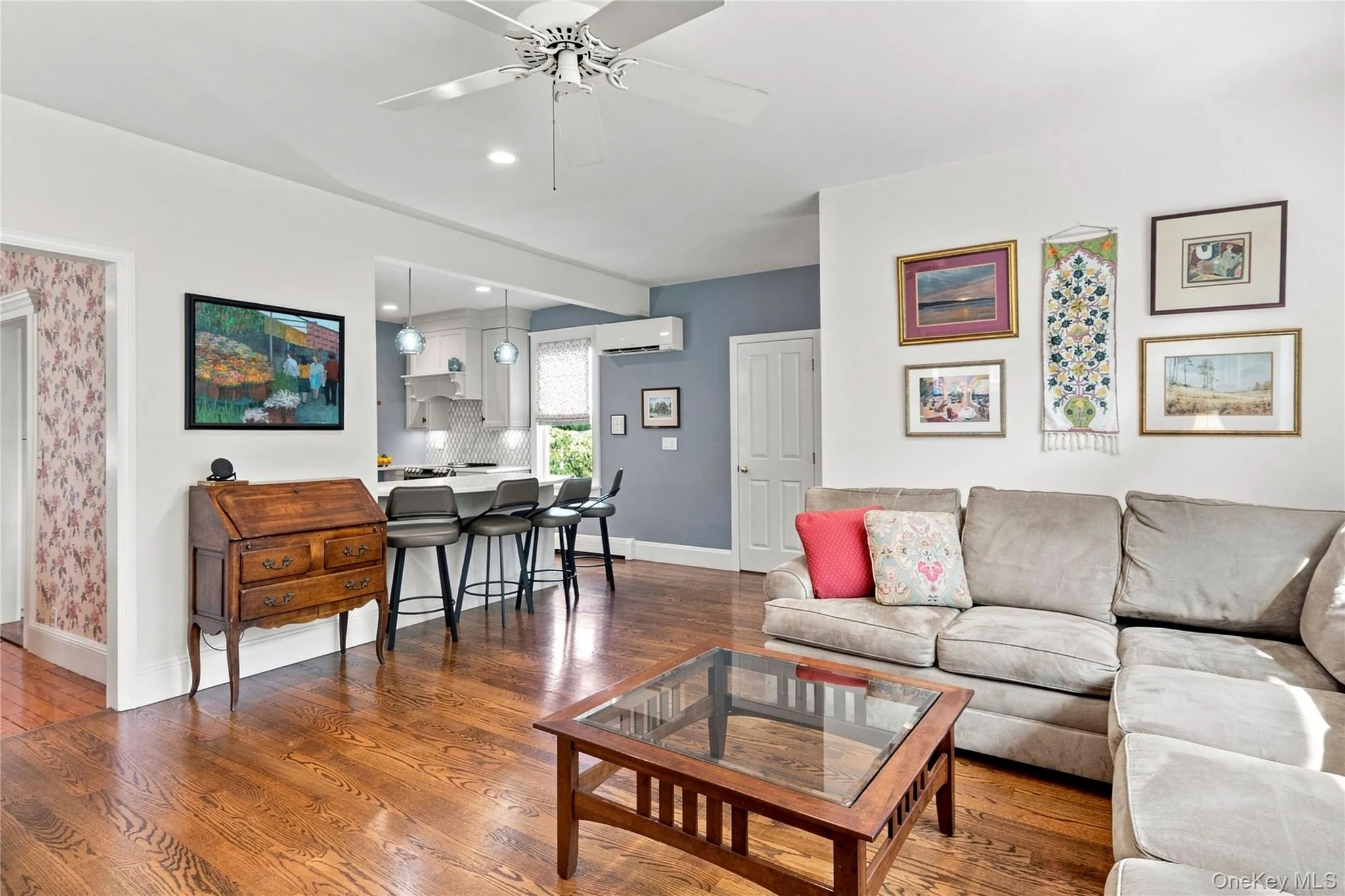 Hardwood flooring throughout, a ceiling fan with light fixture, and an open-concept design to a kitchen featuring a breakfast bar with pendant lighting Hardwood flooring throughout, a ceiling fan with light fixture, and an open-concept design to a kitchen featuring a breakfast bar with pendant lighting