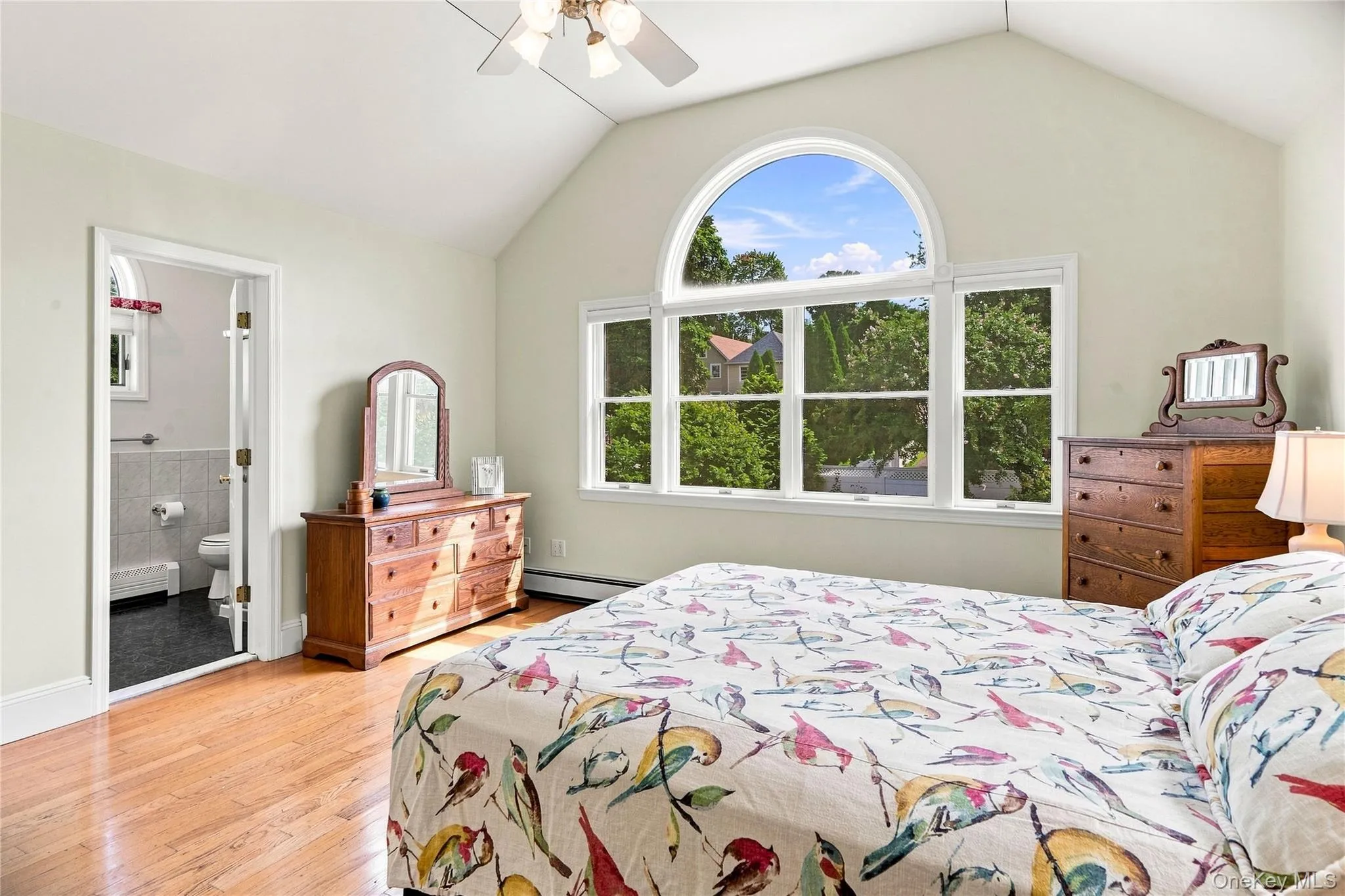 Vaulted ceiling, arched transom window, wood-finish flooring, ceiling fan, and an en-suite bathroom with tiled walls Vaulted ceiling, arched transom window, wood-finish flooring, ceiling fan, and an en-suite bathroom with tiled walls