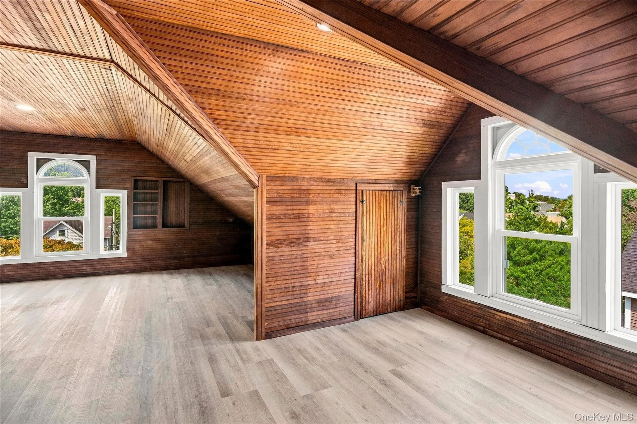 Sloped wood-paneled ceilings, wood-finish flooring, built-in shelving, and white-framed windows with arched transoms Sloped wood-paneled ceilings, wood-finish flooring, built-in shelving, and white-framed windows with arched transoms