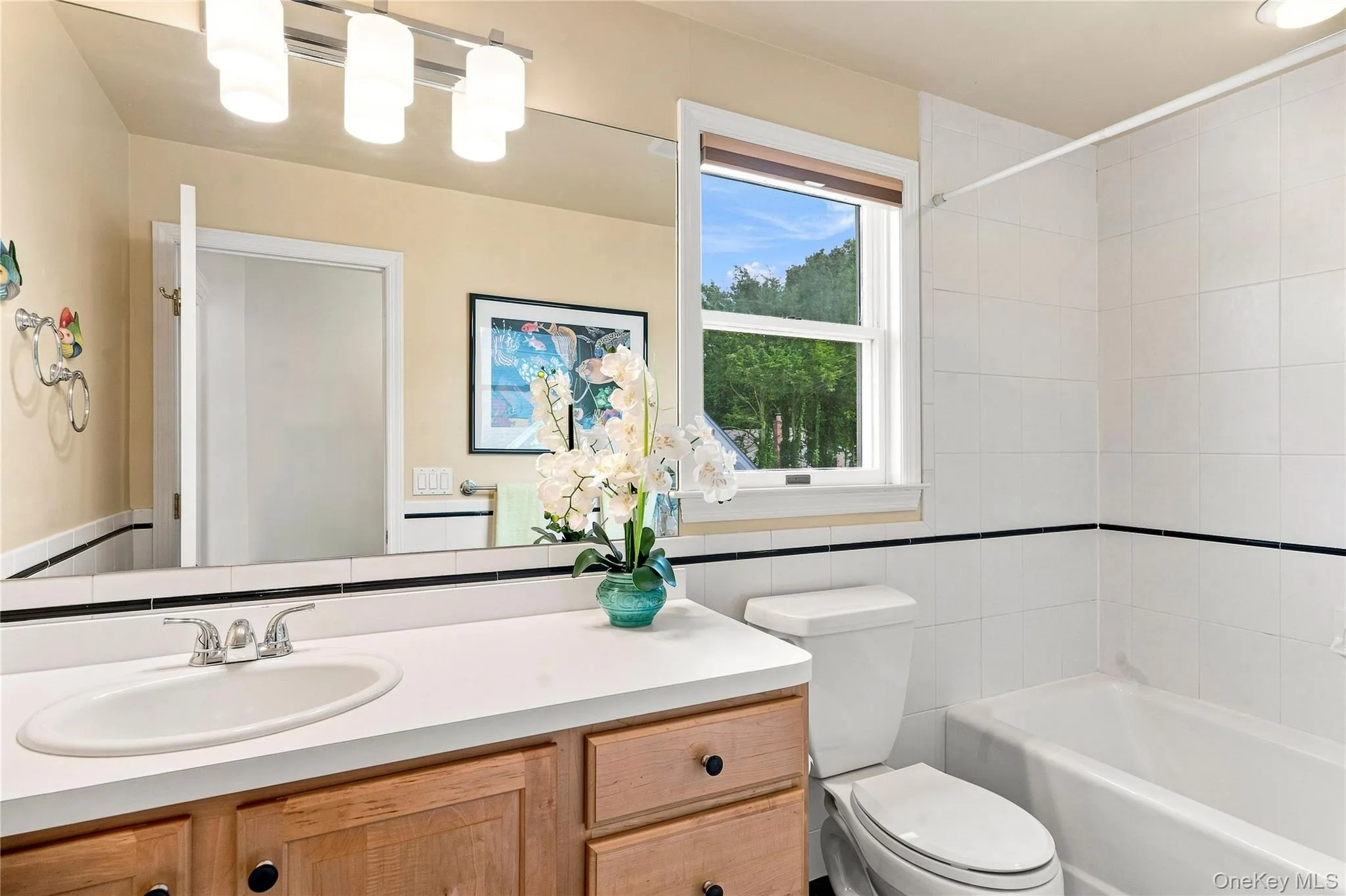 Spacious vanity with a wide mirror, light wood-finish cabinetry, and a white countertop Spacious vanity with a wide mirror, light wood-finish cabinetry, and a white countertop