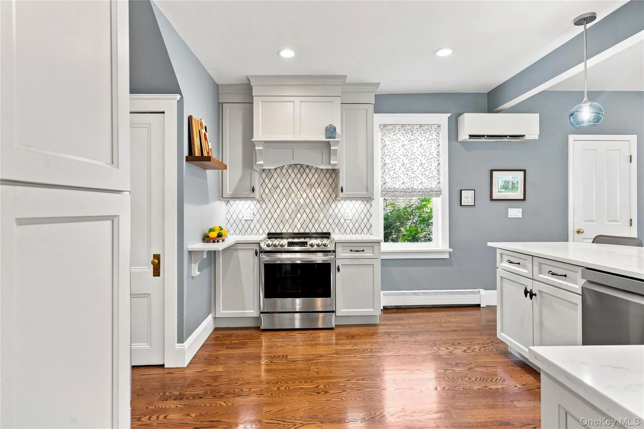 Hardwood flooring, white cabinetry, stainless steel range, patterned Marble backsplash, and a built-in dishwasher Hardwood flooring, white cabinetry, stainless steel range, patterned Marble backsplash, and a built-in dishwasher