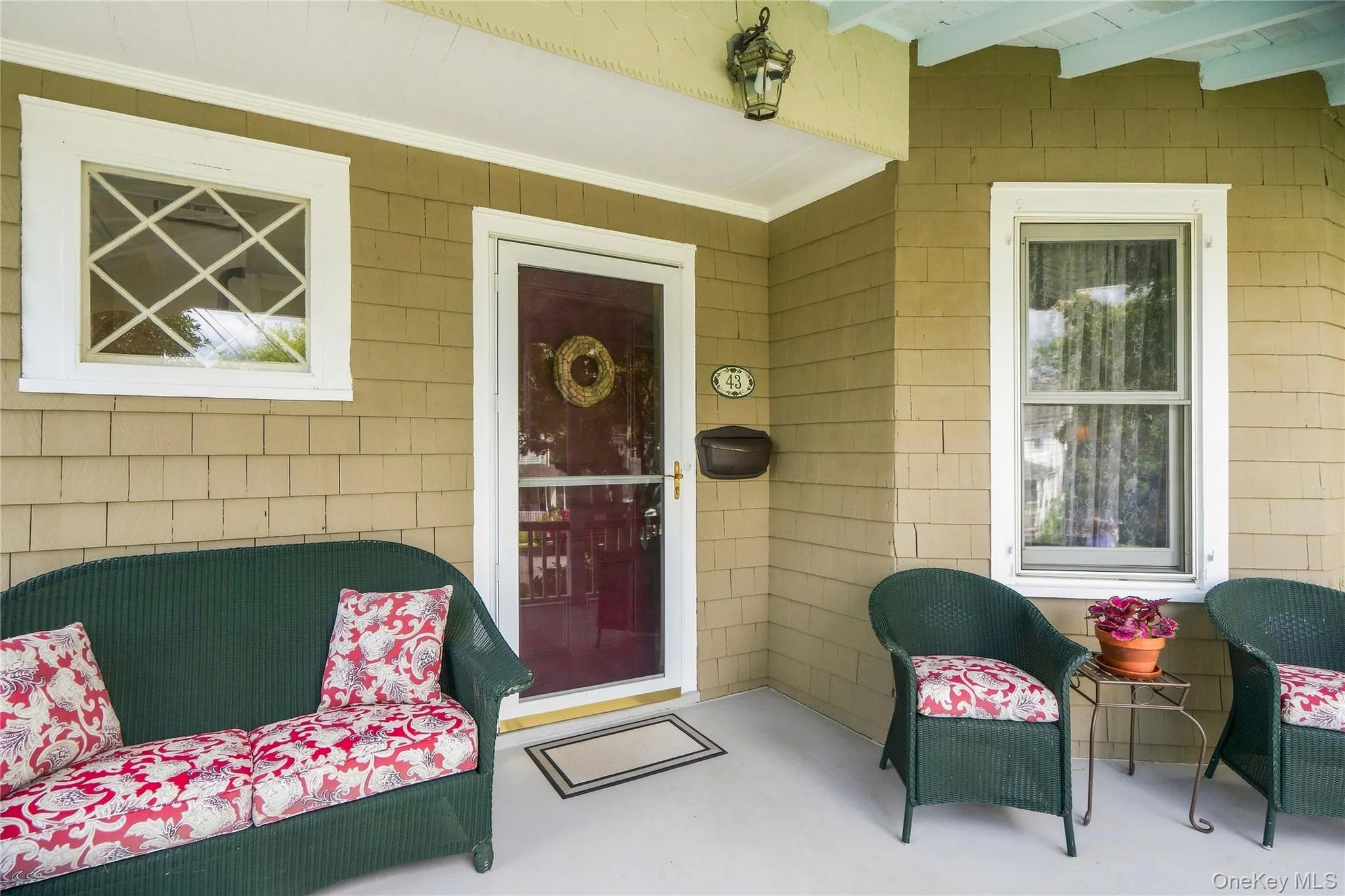 Covered porch with shingle siding, an ornate exterior light fixture, and a red entry door Covered porch with shingle siding, an ornate exterior light fixture, and a red entry door