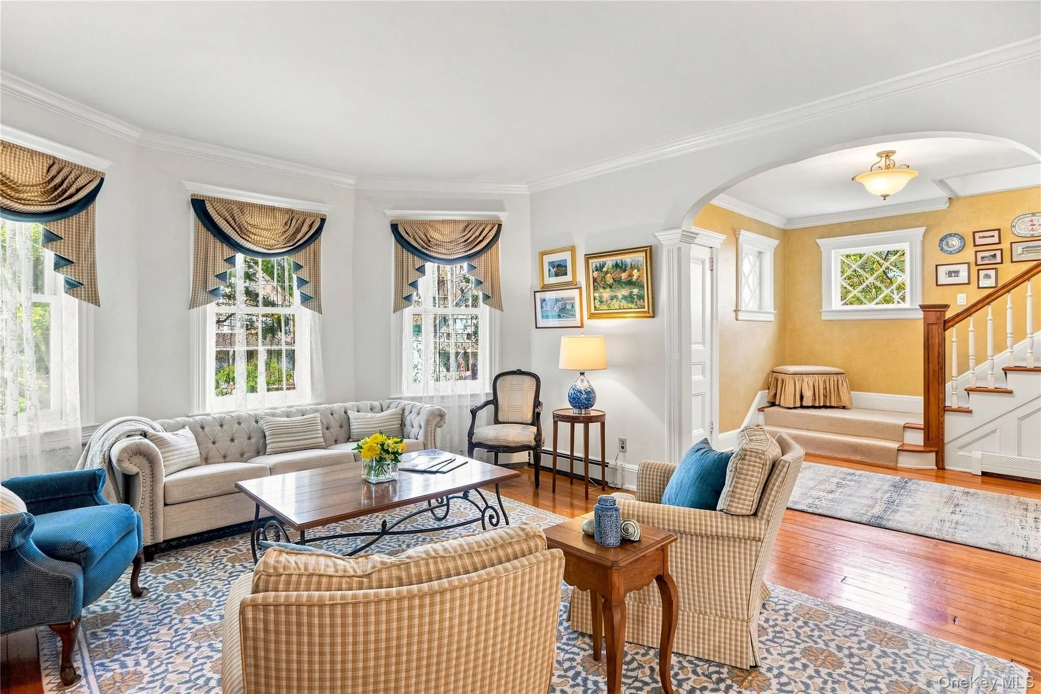 Recessed bay windows with custom valances, an arched entryway, wood flooring, and a detailed staircase with a wood handrail Recessed bay windows with custom valances, an arched entryway, wood flooring, and a detailed staircase with a wood handrail