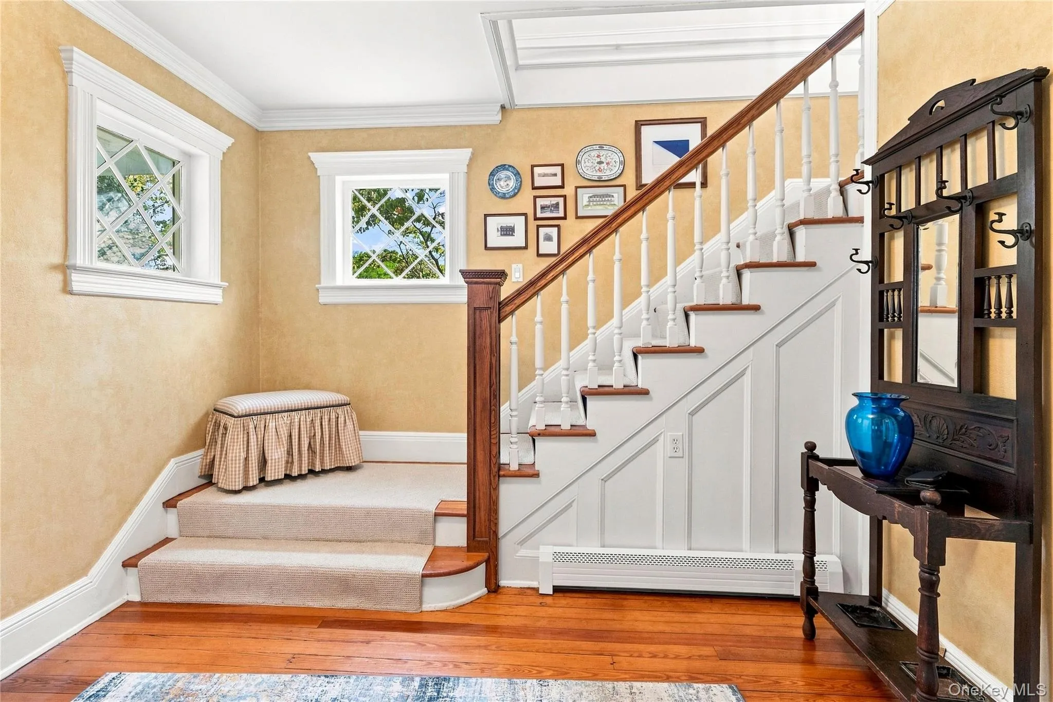 Hardwood flooring, painted wainscoting, carpeted stairs, two windows with decorative muntins, and a wood railing with white balusters Hardwood flooring, painted wainscoting, carpeted stairs, two windows with decorative muntins, and a wood railing with white balusters
