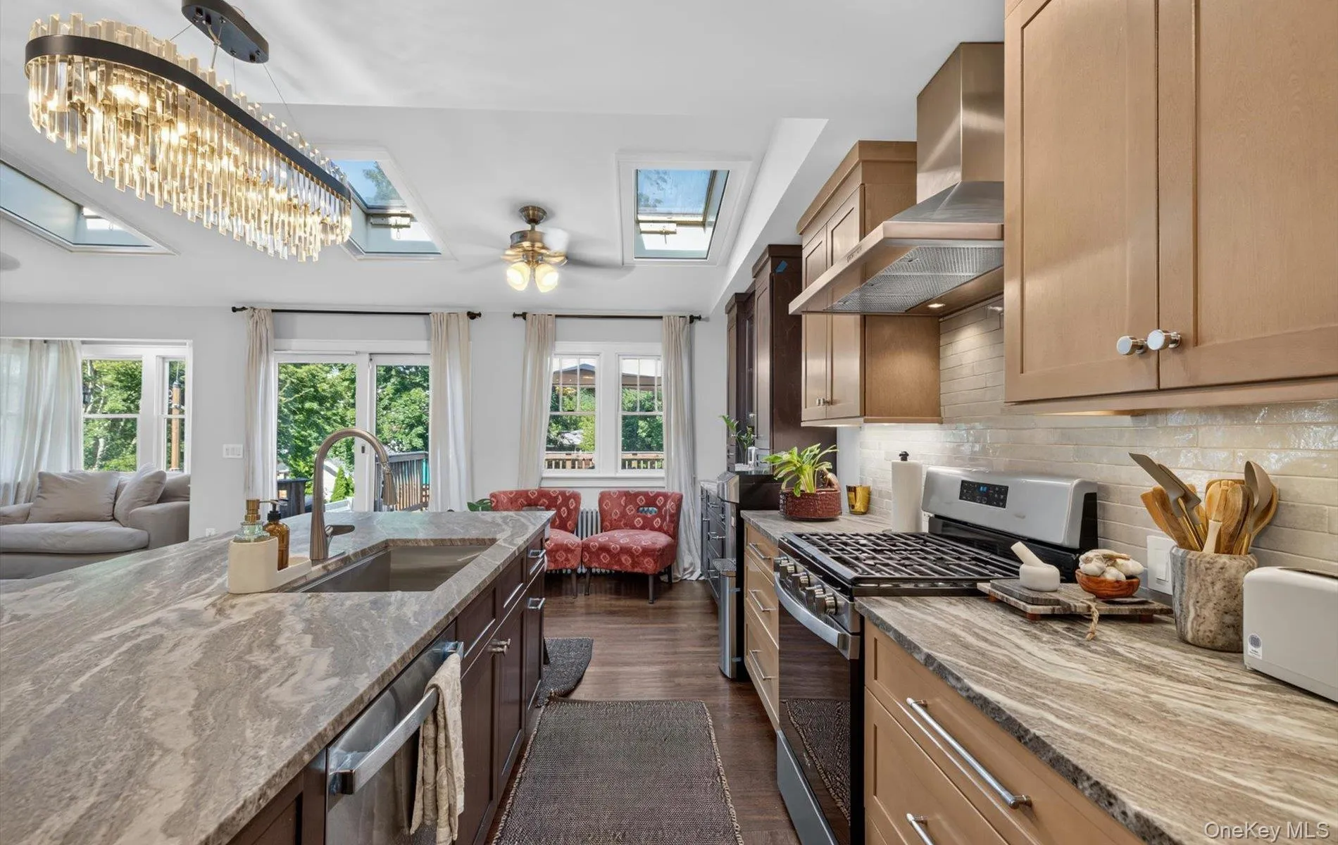 Kitchen featuring a large island with an undermount sink, stainless steel appliances, a tiled backsplash, wood-finish cabinetry, and multiple skylights Kitchen featuring a large island with an undermount sink, stainless steel appliances, a tiled backsplash, wood-finish cabinetry, and multiple skylights