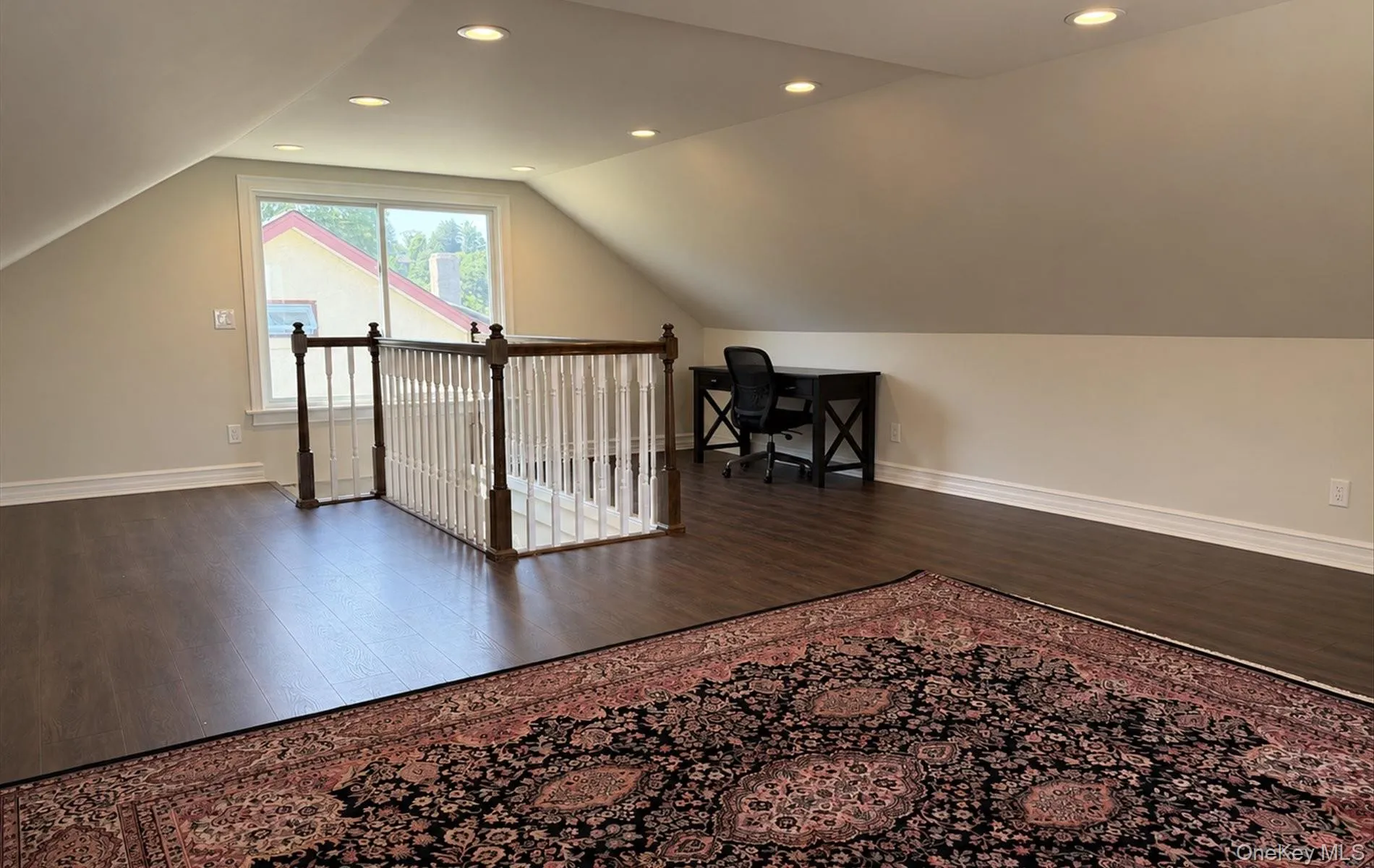 Spacious loft area featuring dark wood-finish flooring, recessed lighting, and a white baluster staircase with a dark wood handrail Spacious loft area featuring dark wood-finish flooring, recessed lighting, and a white baluster staircase with a dark wood handrail