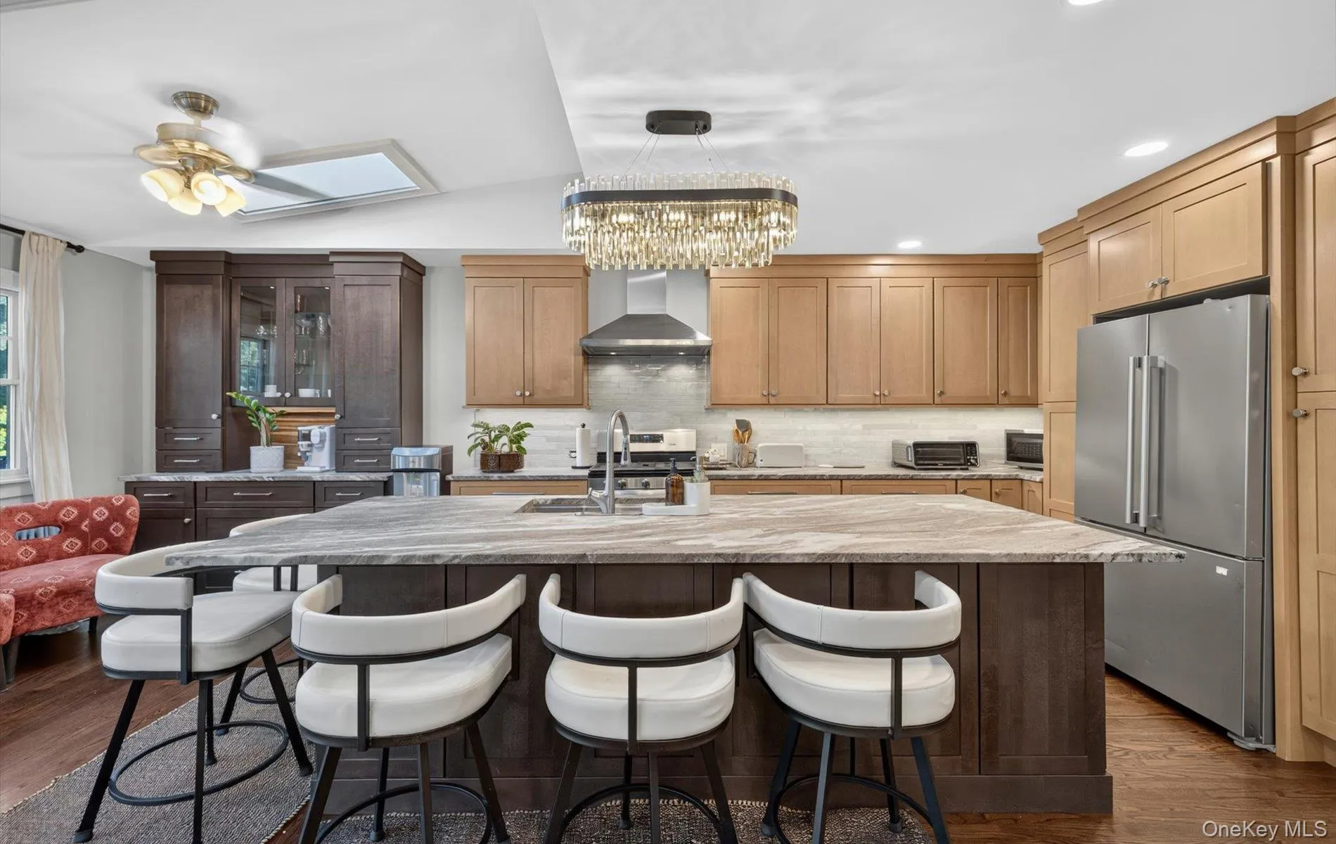 Spacious kitchen featuring a large central island with seating, a stainless steel refrigerator, and ample cabinetry in varying finishes Spacious kitchen featuring a large central island with seating, a stainless steel refrigerator, and ample cabinetry in varying finishes