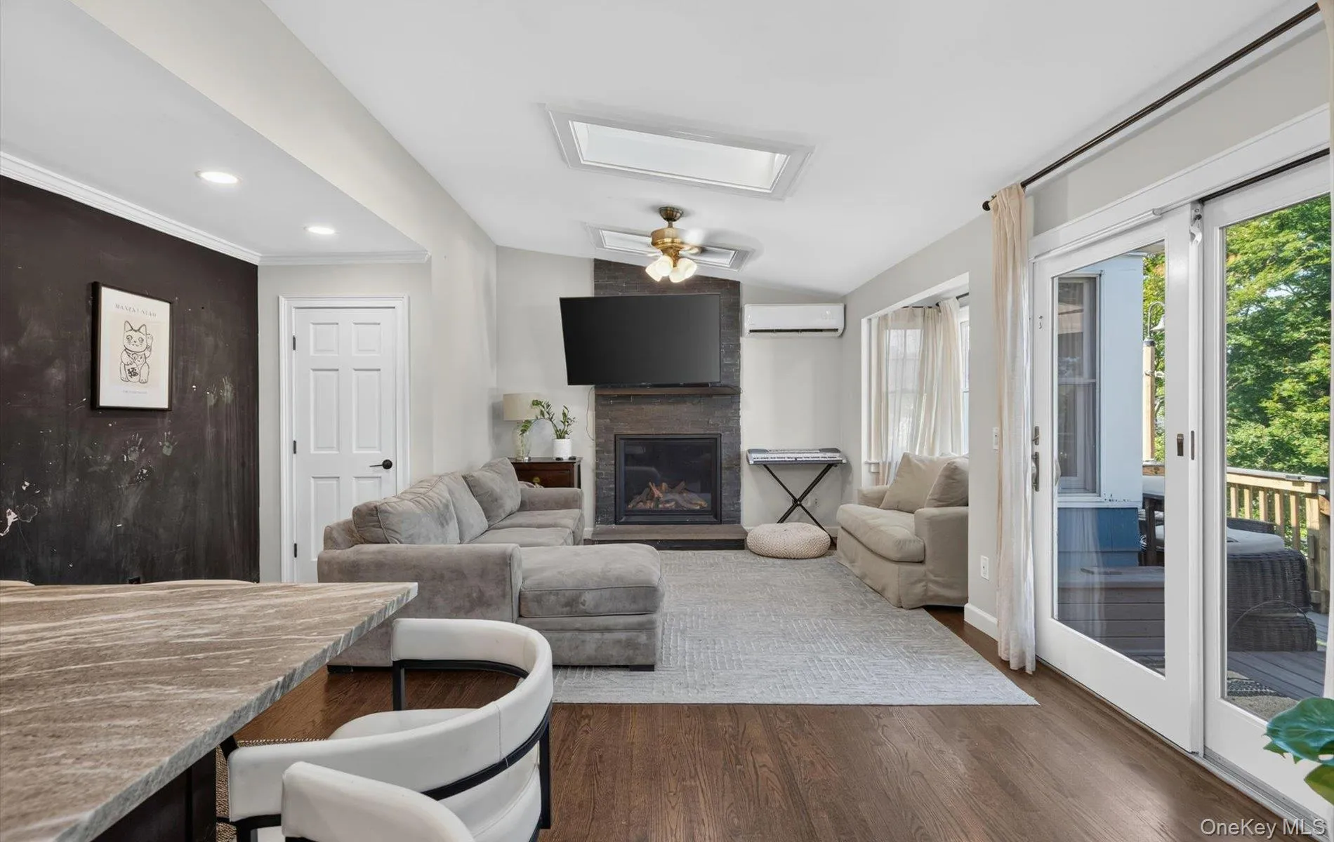 Family room featuring a stone-clad fireplace, wood-finish flooring, and a skylight, sliding french doors to expansive Deck Family room featuring a stone-clad fireplace, wood-finish flooring, and a skylight, sliding french doors to expansive Deck