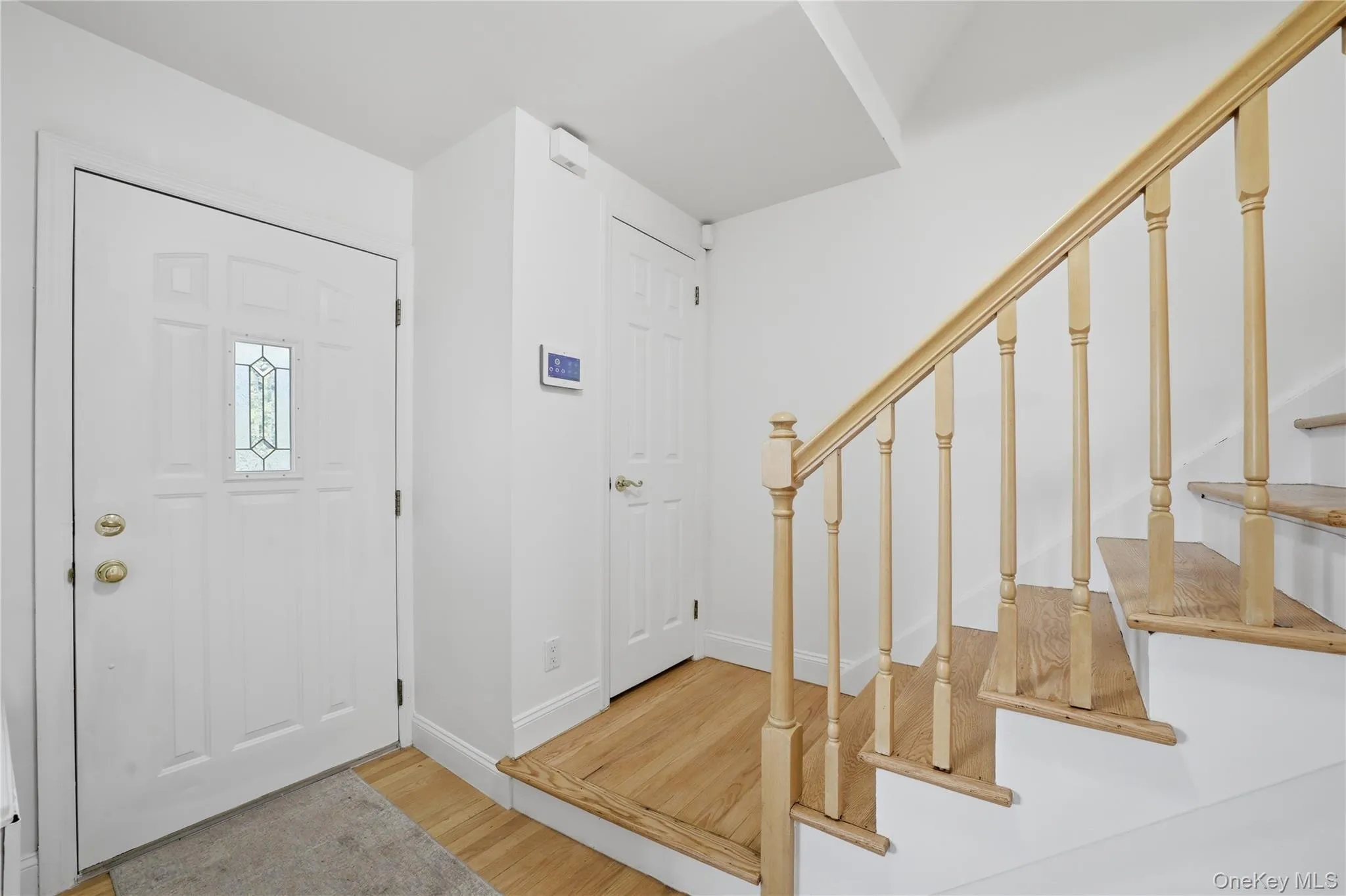 Entryway featuring a paneled door with decorative glass inlay, hardwood flooring, and a staircase with a natural wood handrail and balusters Entryway featuring a paneled door with decorative glass inlay, hardwood flooring, and a staircase with a natural wood handrail and balusters