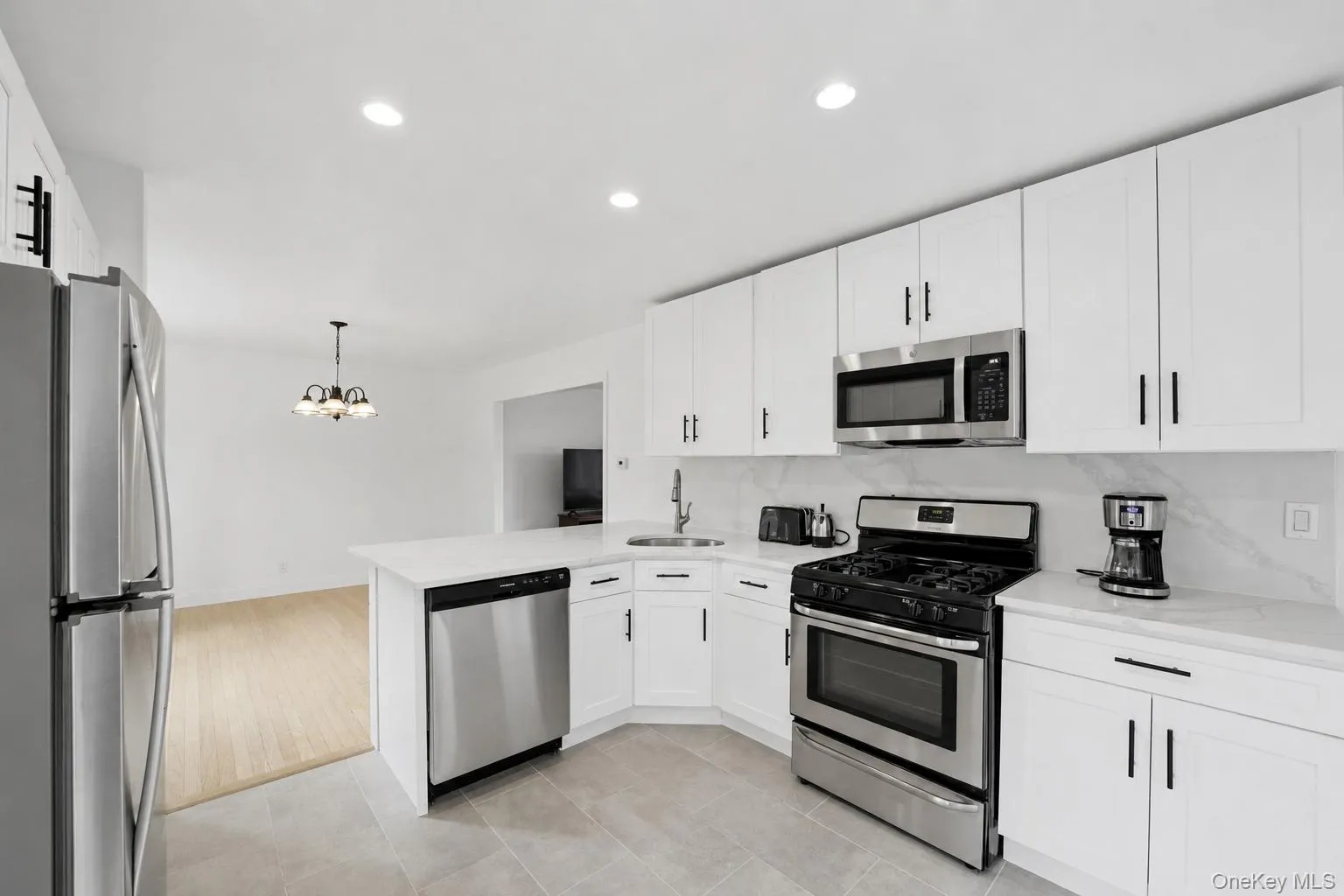 Modern kitchen featuring white cabinetry with black hardware, stainless steel appliances, a white countertop, and a tile backsplash Modern kitchen featuring white cabinetry with black hardware, stainless steel appliances, a white countertop, and a tile backsplash