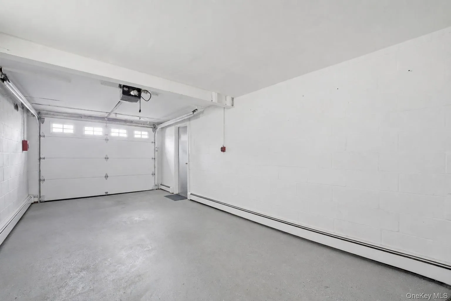 Attached garage space featuring a paneled garage door with upper window inserts, an automatic opener, concrete flooring, and painted cinder block walls Attached garage space featuring a paneled garage door with upper window inserts, an automatic opener, concrete flooring, and painted cinder block walls