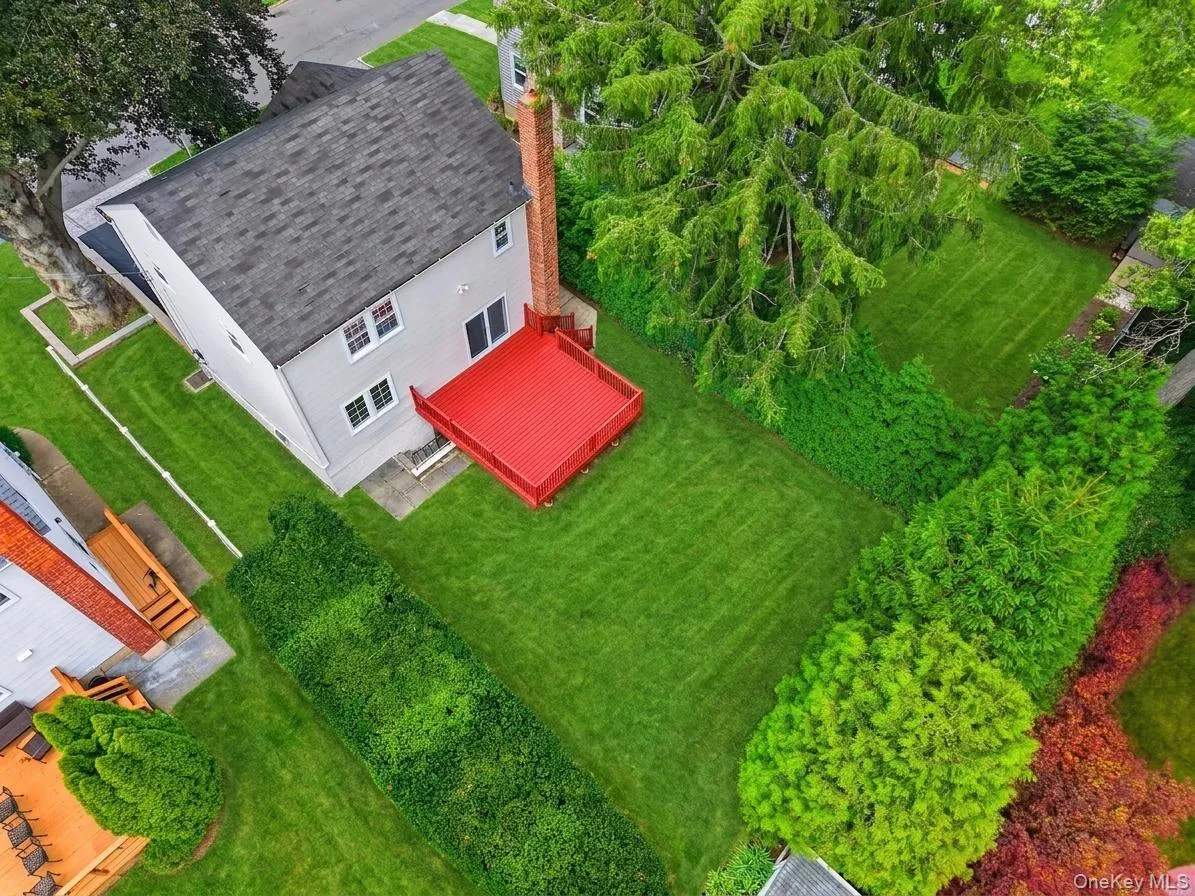 Expansive backyard featuring a vibrant red deck, manicured lawn, established landscaping, and mature perimeter trees Expansive backyard featuring a vibrant red deck, manicured lawn, established landscaping, and mature perimeter trees