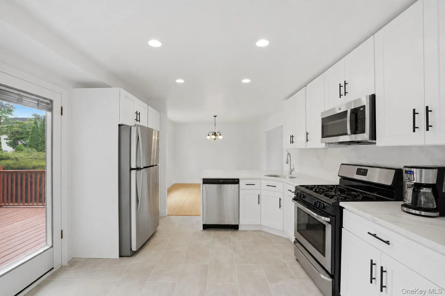Contemporary kitchen featuring white cabinetry with black hardware, stainless steel appliances, light-toned countertops, and recessed lighting Contemporary kitchen featuring white cabinetry with black hardware, stainless steel appliances, light-toned countertops, and recessed lighting