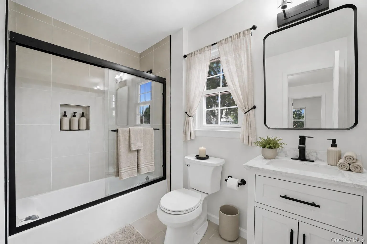 Bathroom featuring a white vanity with a light-toned countertop, a black-framed mirror, and a window with white trim Bathroom featuring a white vanity with a light-toned countertop, a black-framed mirror, and a window with white trim