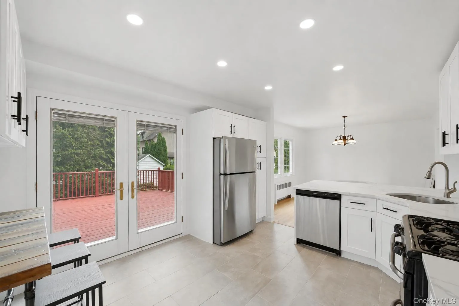 Spacious kitchen featuring white cabinetry, stainless steel appliances, light-toned flooring, recessed lighting, and double glass doors opening to a red-stained deck Spacious kitchen featuring white cabinetry, stainless steel appliances, light-toned flooring, recessed lighting, and double glass doors opening to a red-stained deck