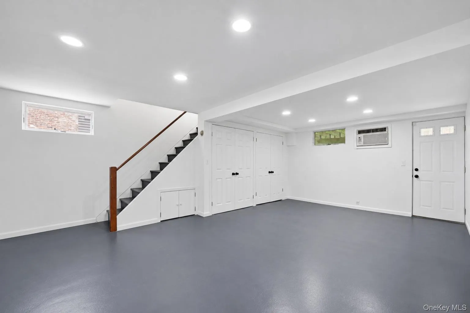Expansive basement-level space featuring recessed lighting, a finished staircase with wood handrail, multiple storage closets with bifold doors, and a paneled entry door Expansive basement-level space featuring recessed lighting, a finished staircase with wood handrail, multiple storage closets with bifold doors, and a paneled entry door
