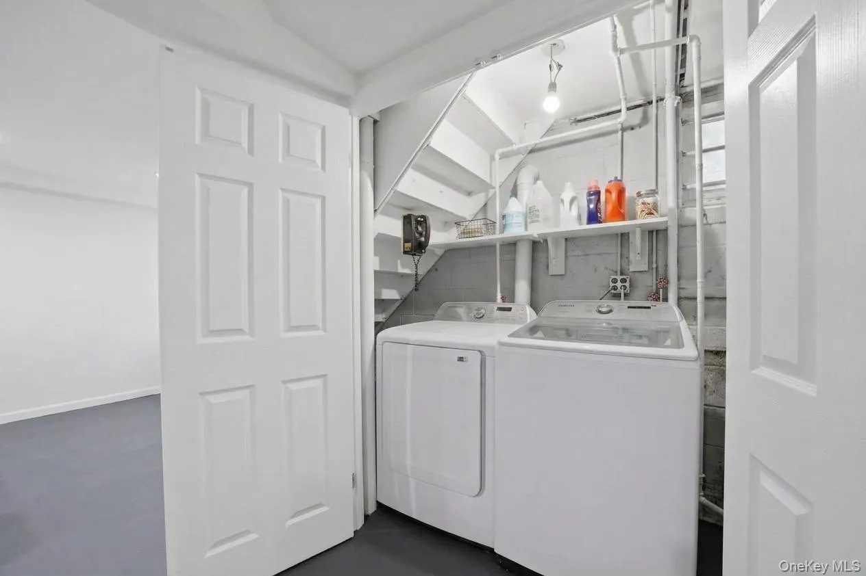 Dedicated laundry area featuring a washer and dryer, under-stair storage shelving, and exposed utility piping Dedicated laundry area featuring a washer and dryer, under-stair storage shelving, and exposed utility piping