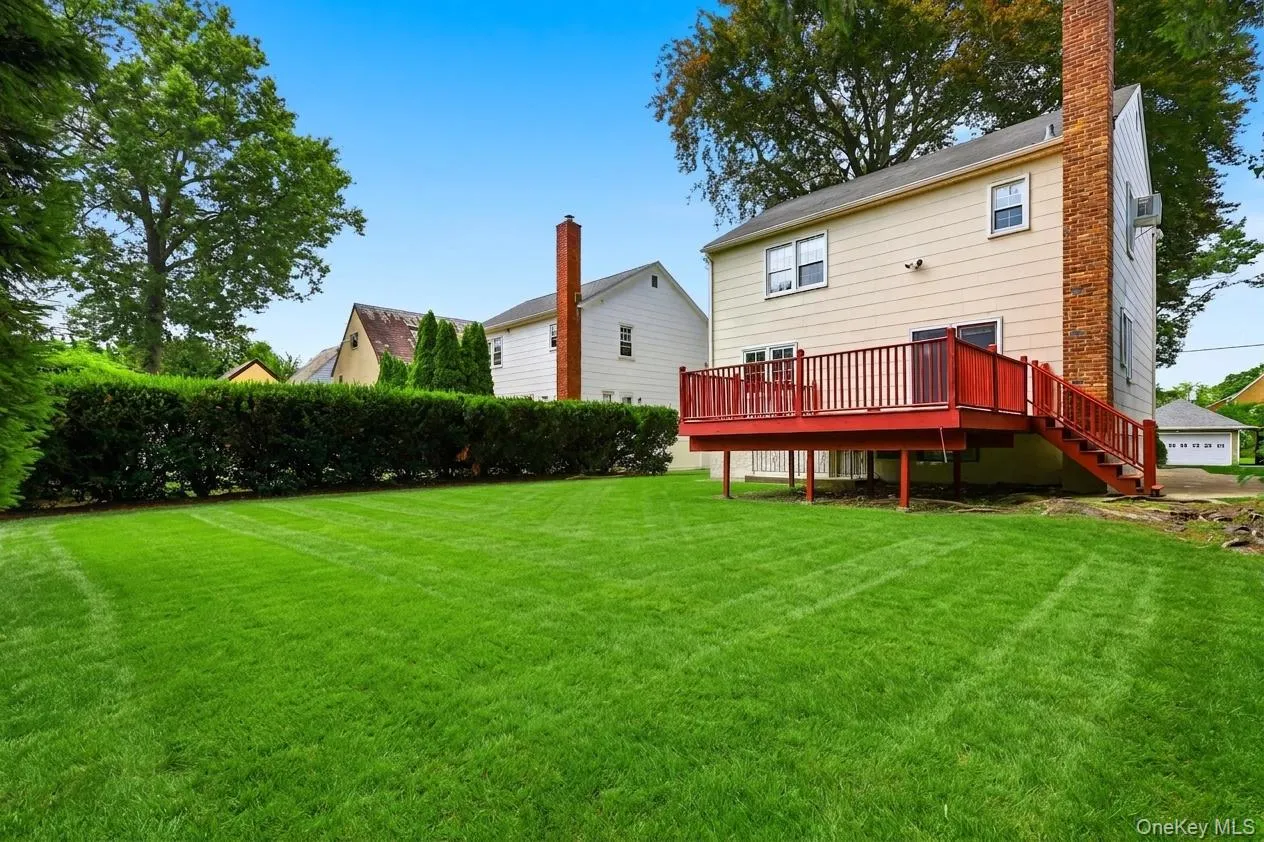 Expansive green lawn featuring a privacy hedge, a multi-level wood deck with painted railings, and an exterior brick chimney Expansive green lawn featuring a privacy hedge, a multi-level wood deck with painted railings, and an exterior brick chimney