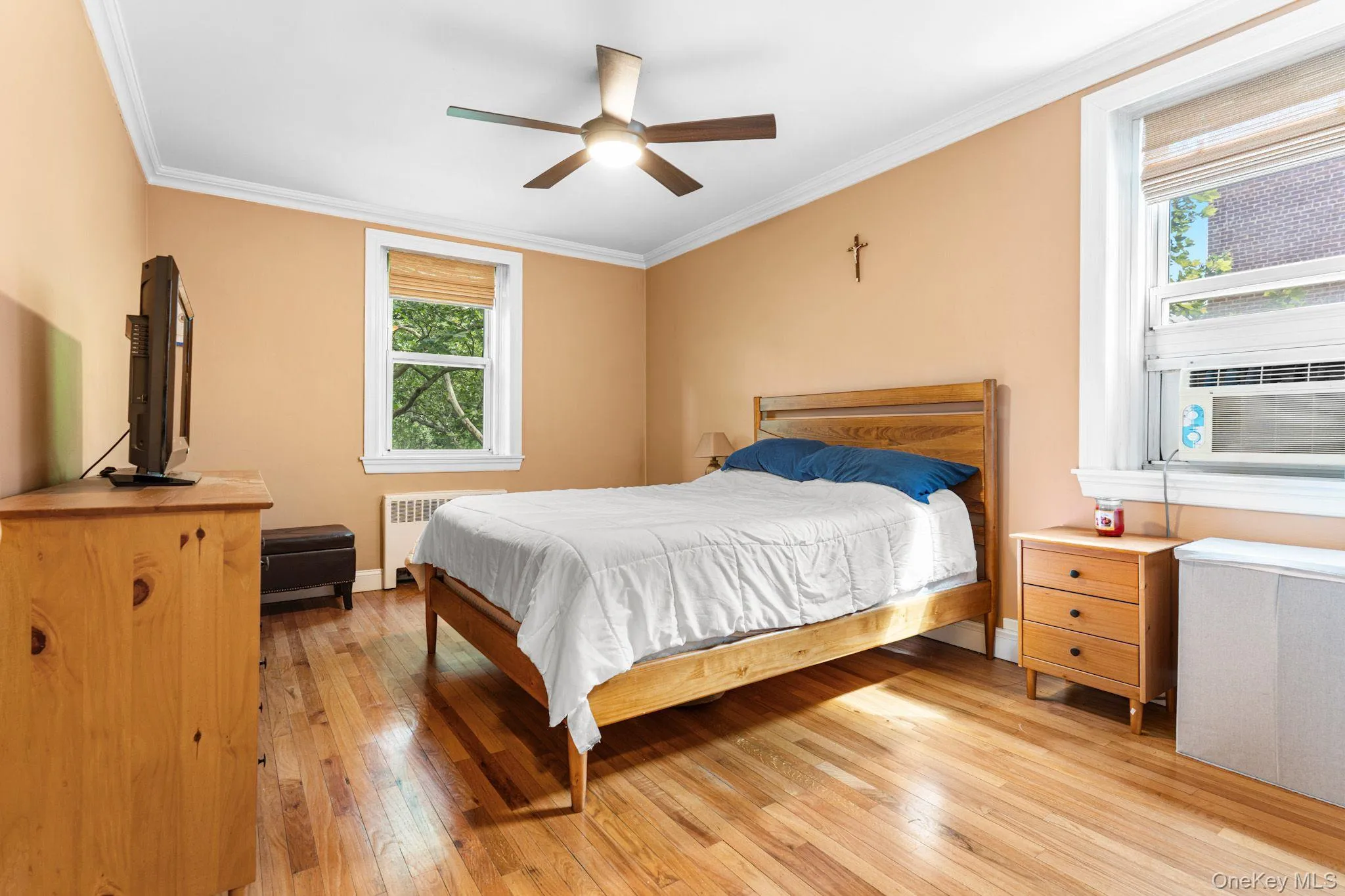 Bedroom featuring wood-finish flooring, crown molding, and two windows with natural light Bedroom featuring wood-finish flooring, crown molding, and two windows with natural light