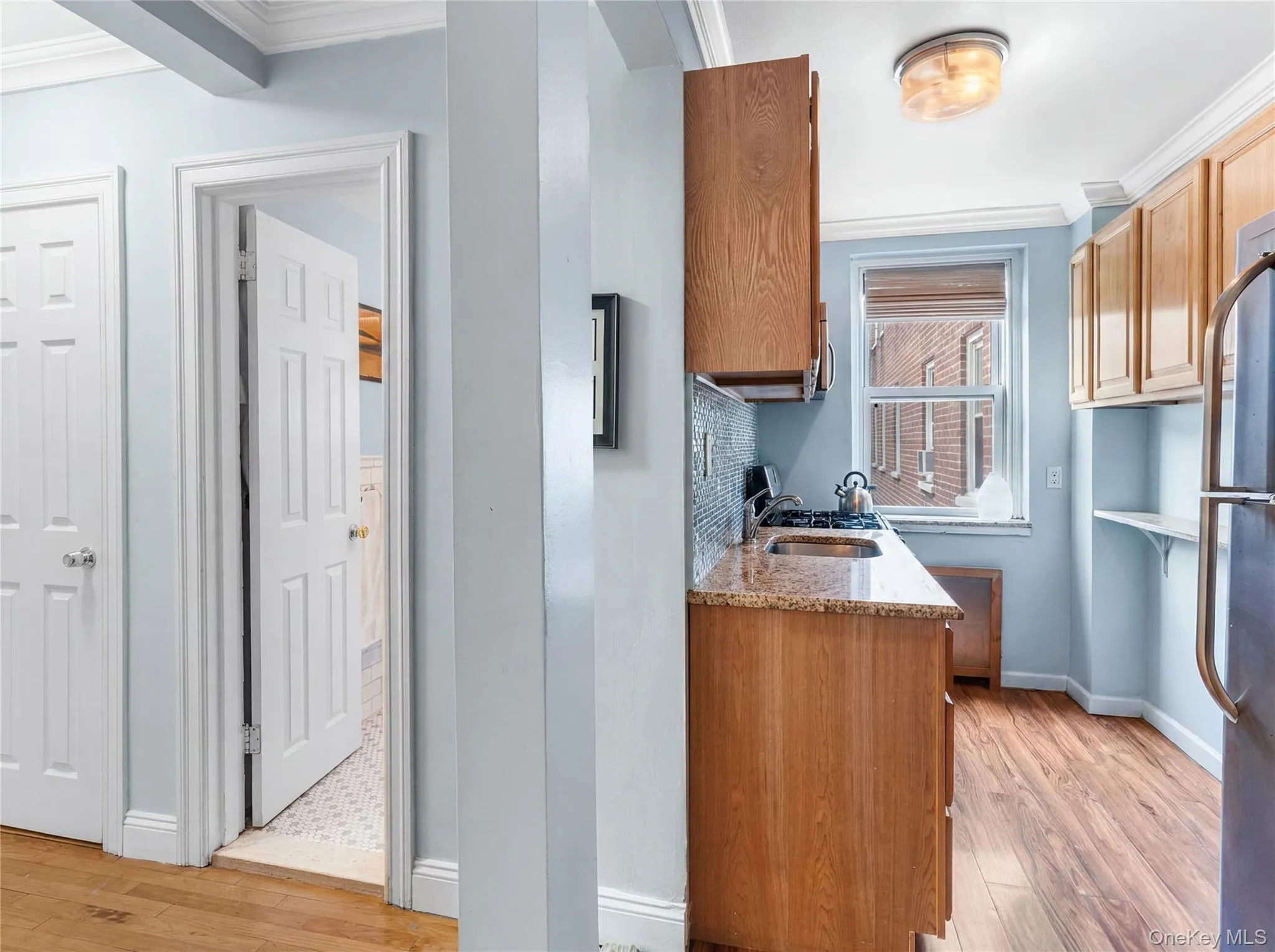 Compact kitchen featuring wood-finish cabinetry, granite-style countertops, a mosaic tile backsplash, and a window providing natural light Compact kitchen featuring wood-finish cabinetry, granite-style countertops, a mosaic tile backsplash, and a window providing natural light