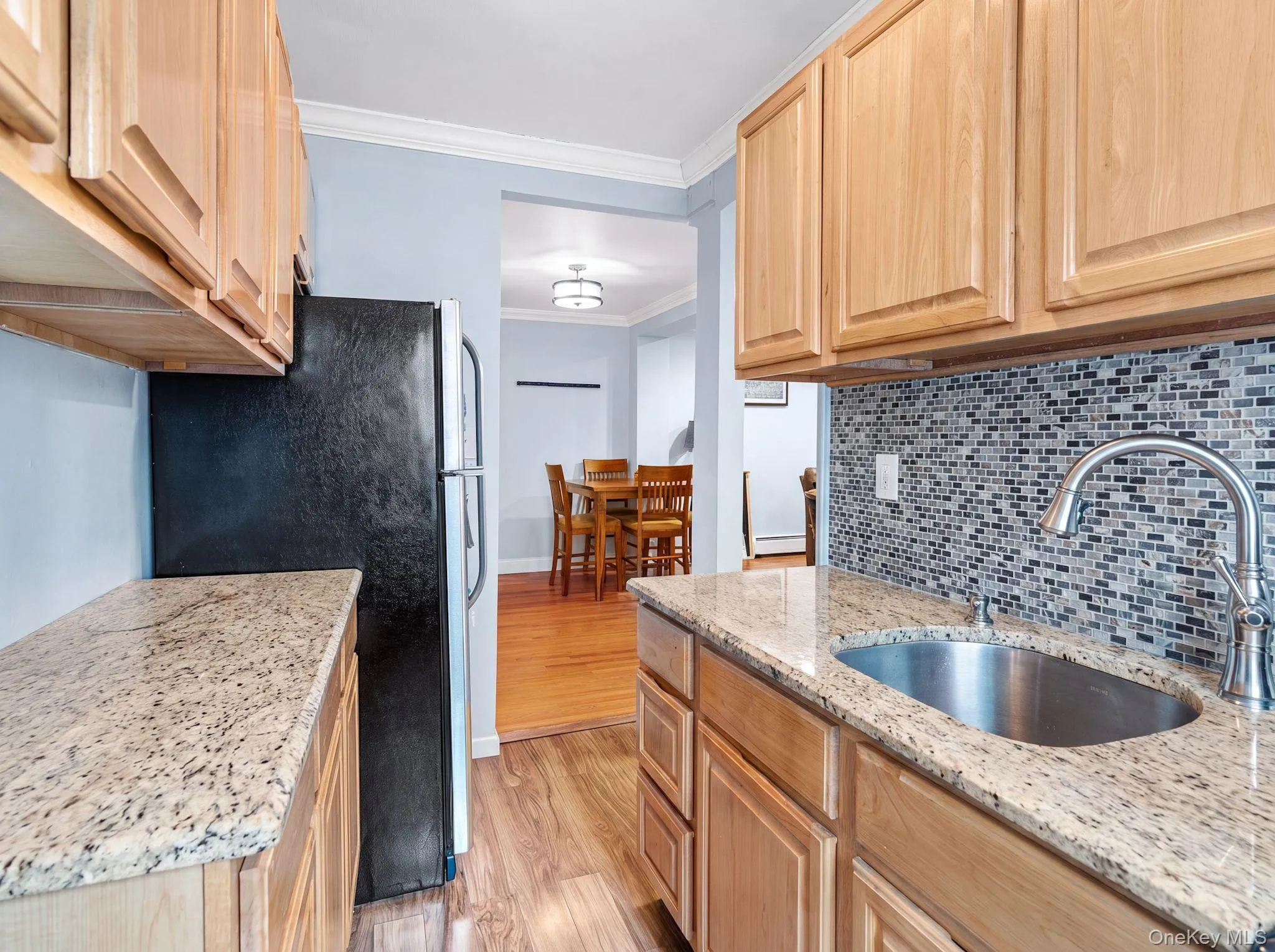 Compact kitchen featuring wood-finish cabinetry, granite-style countertops, a mosaic tile backsplash, and a window providing natural light Compact kitchen featuring wood-finish cabinetry, granite-style countertops, a mosaic tile backsplash, and a window providing natural light