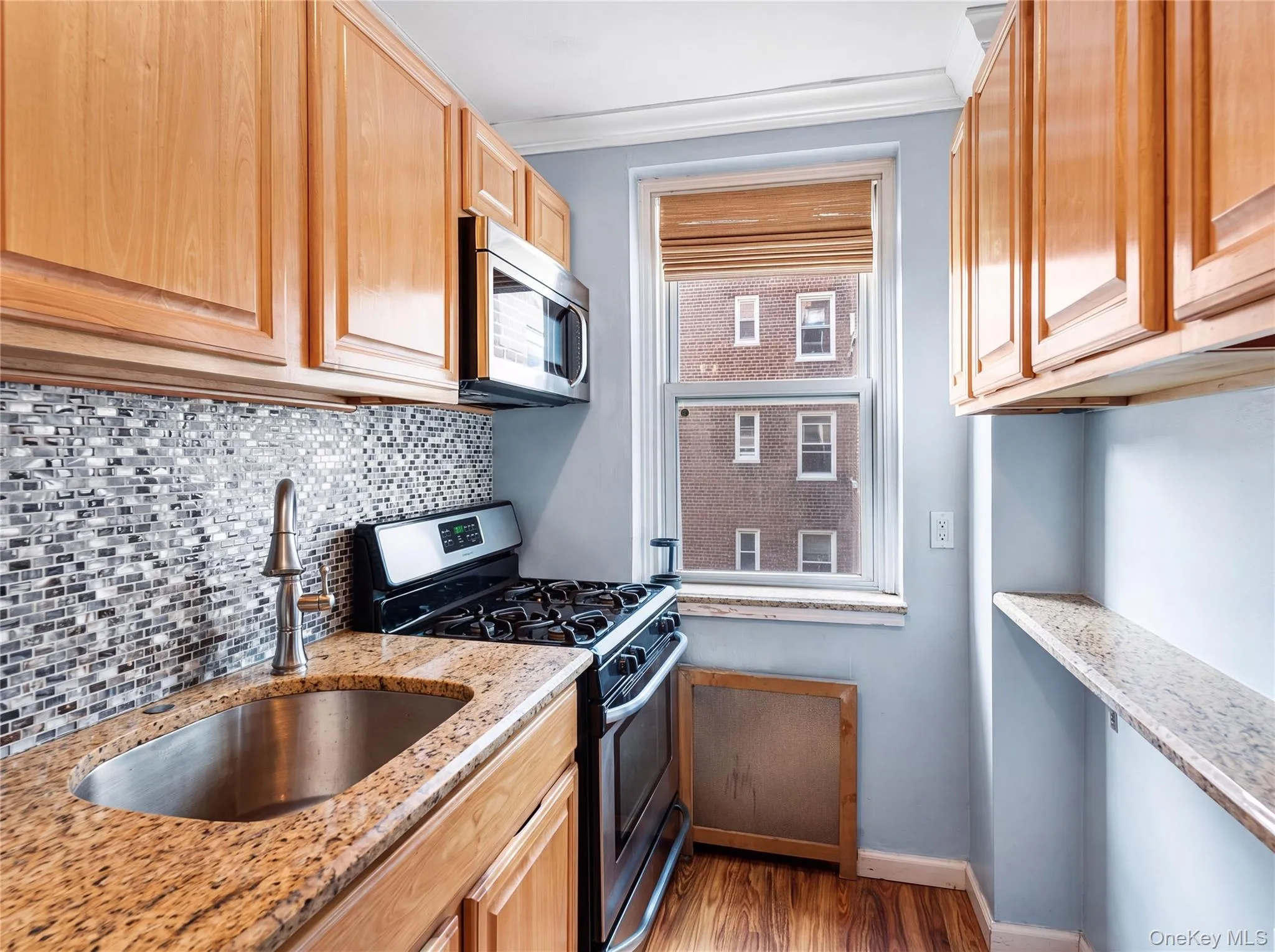 Compact kitchen featuring wood-finish cabinetry, granite-style countertops, a mosaic tile backsplash, and a window providing natural light Compact kitchen featuring wood-finish cabinetry, granite-style countertops, a mosaic tile backsplash, and a window providing natural light
