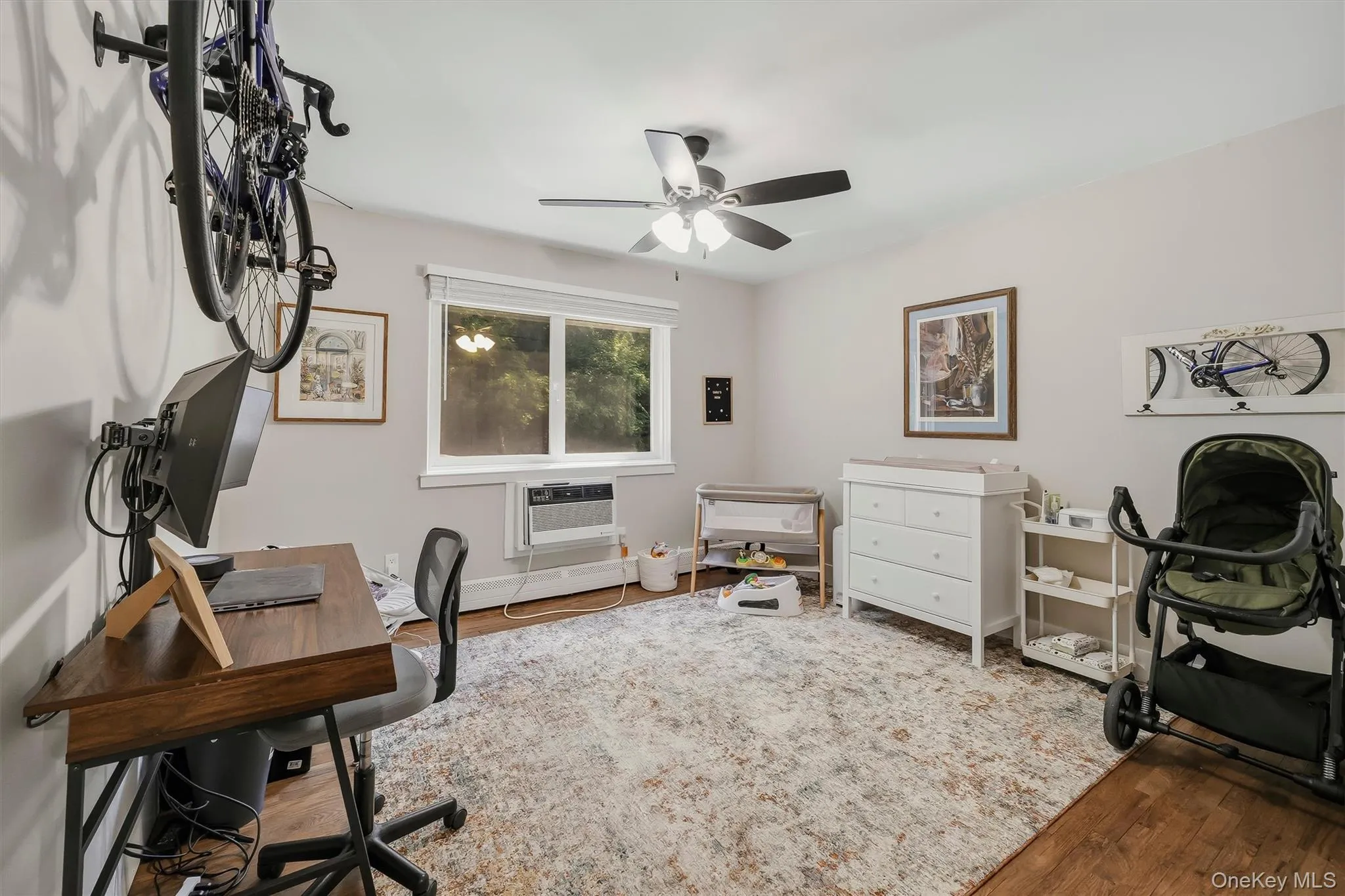 Versatile secondary bedroom or home office featuring hardwood flooring, ceiling fan with integrated lighting, large window with natural light, and ample wall space for storage or display Versatile secondary bedroom or home office featuring hardwood flooring, ceiling fan with integrated lighting, large window with natural light, and ample wall space for storage or display