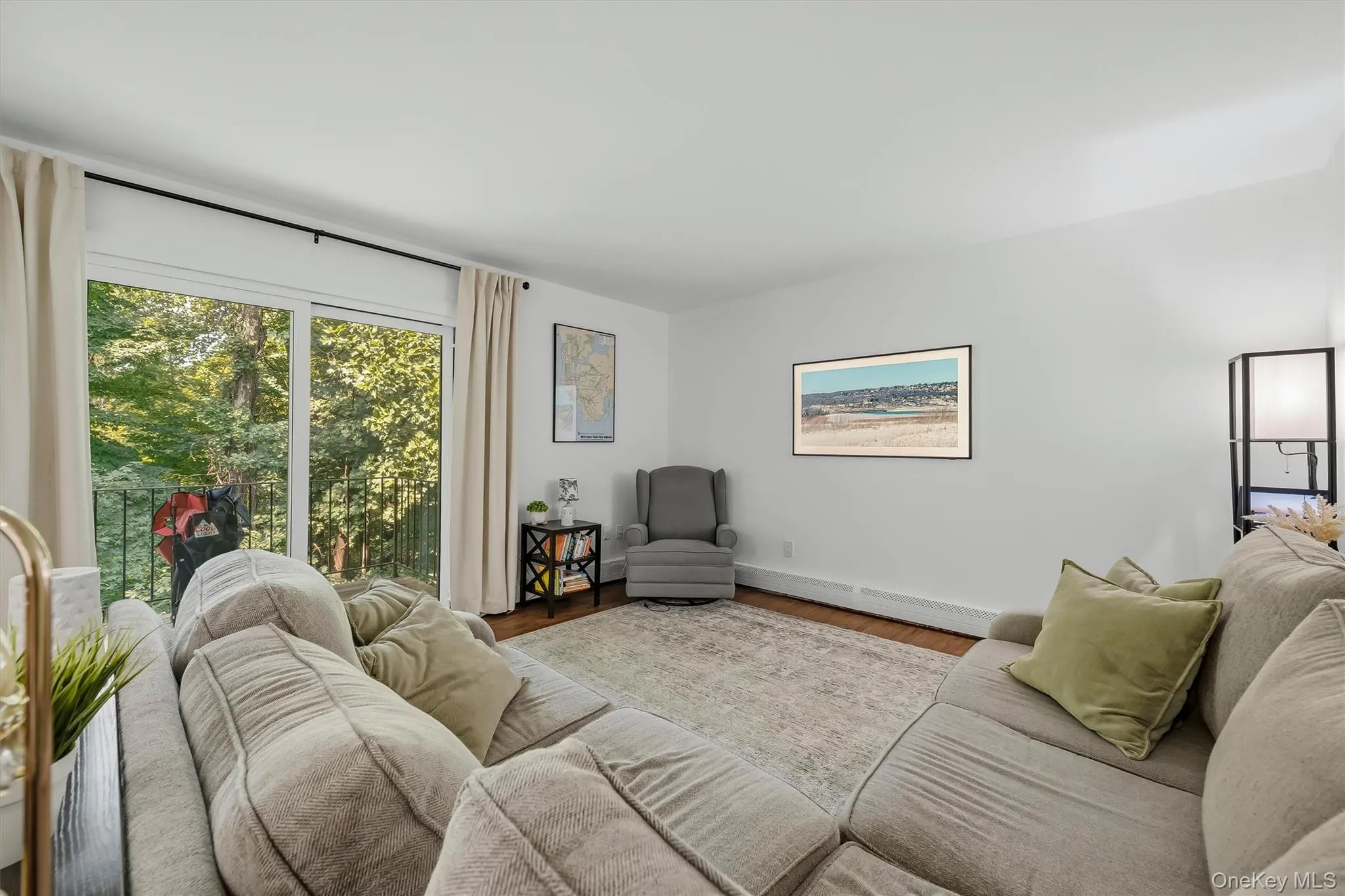 Bright, light-filled living room showcasing large multi-pane windows with natural woodland views, neutral striped upholstery seating, wood-finish flooring, and soft neutral area rug Bright, light-filled living room showcasing large multi-pane windows with natural woodland views, neutral striped upholstery seating, wood-finish flooring, and soft neutral area rug