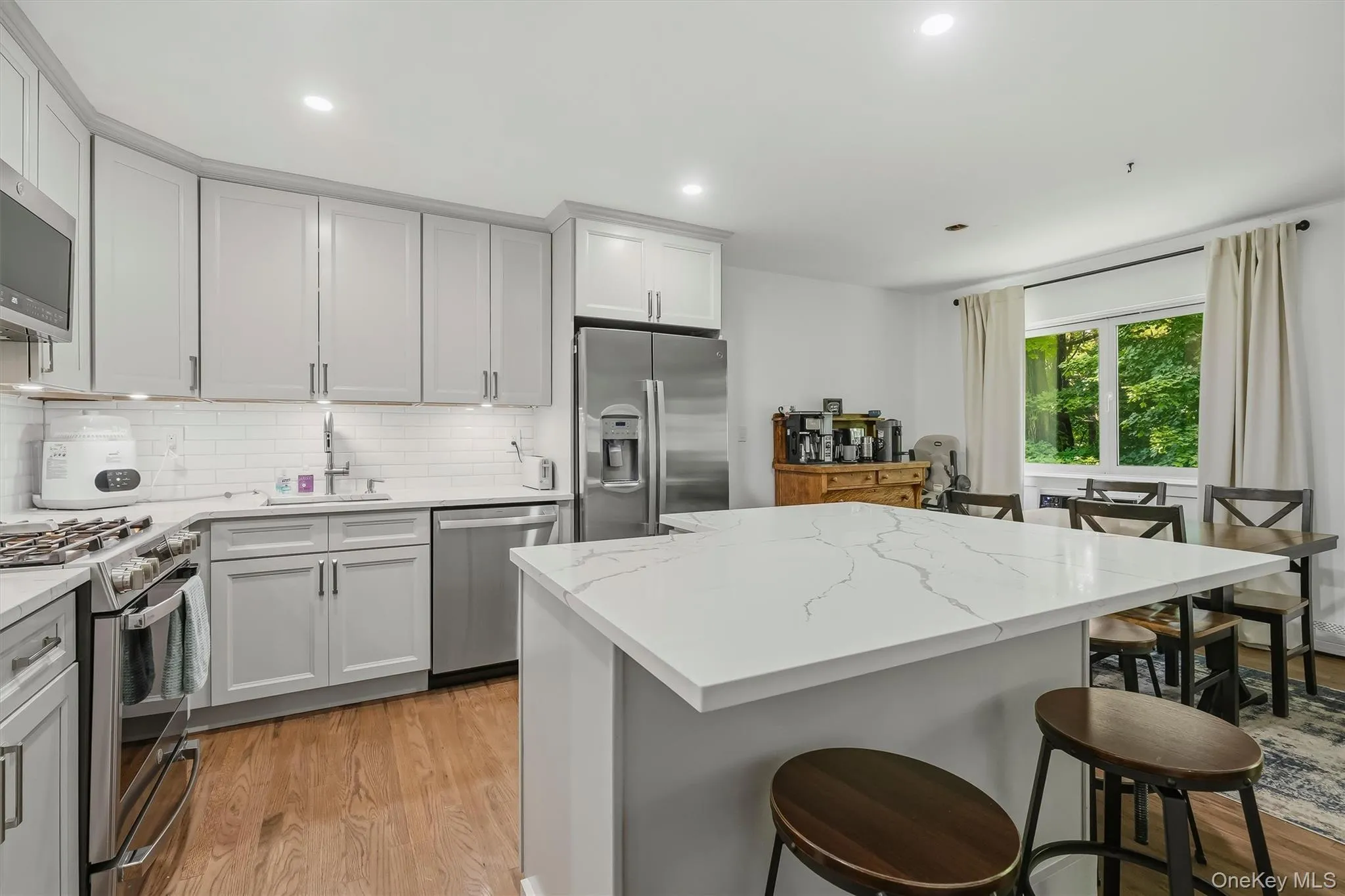Contemporary kitchen featuring white cabinetry with brushed nickel hardware, stainless steel appliances including a gas range and French-door refrigerator, and white subway tile backsplash Contemporary kitchen featuring white cabinetry with brushed nickel hardware, stainless steel appliances including a gas range and French-door refrigerator, and white subway tile backsplash