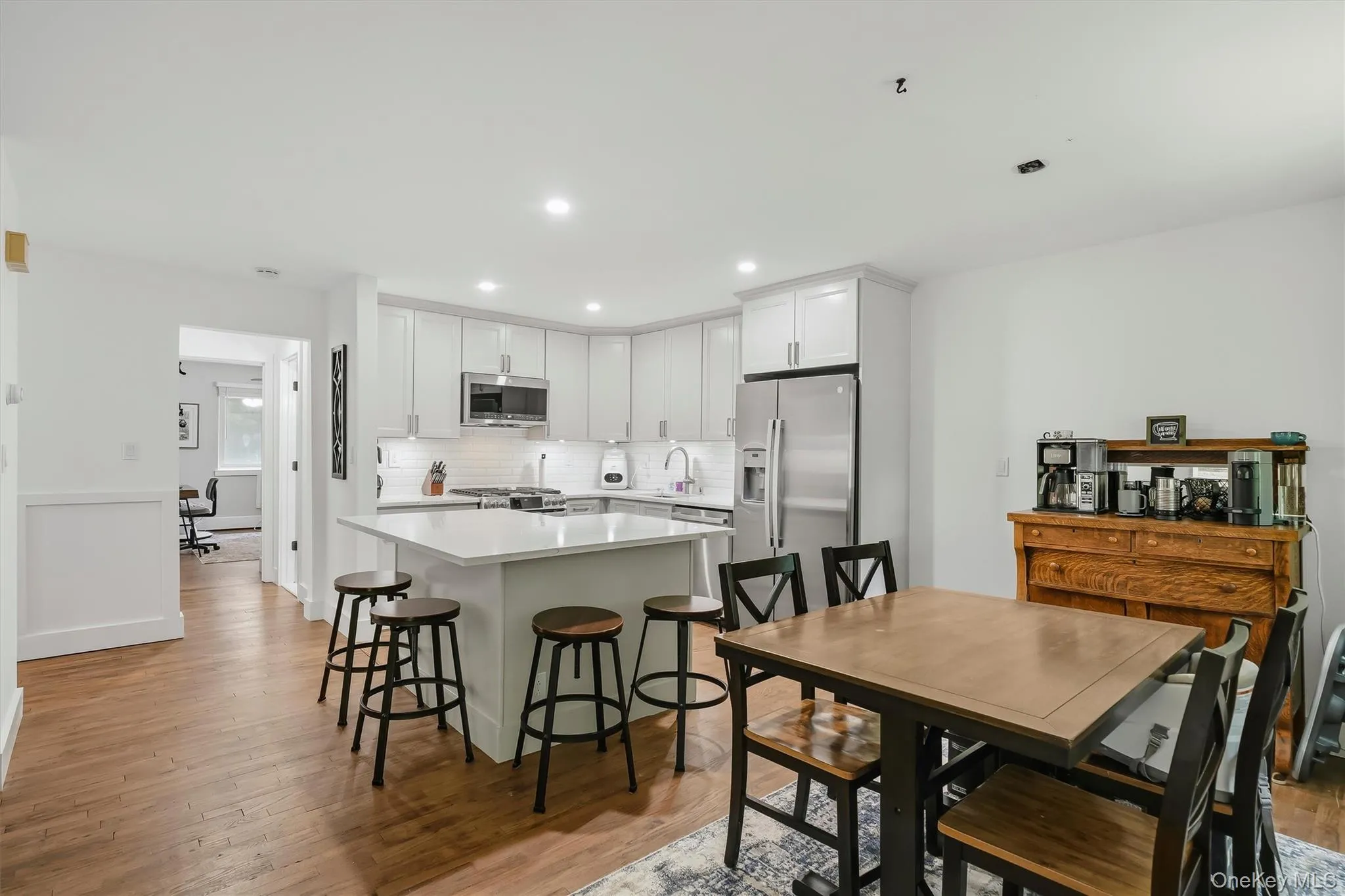 Open-concept kitchen and dining area featuring white cabinetry with stainless steel appliances, a large center island with seating for multiple guests, quartz countertops, and wood-finish flooring throughout Open-concept kitchen and dining area featuring white cabinetry with stainless steel appliances, a large center island with seating for multiple guests, quartz countertops, and wood-finish flooring throughout