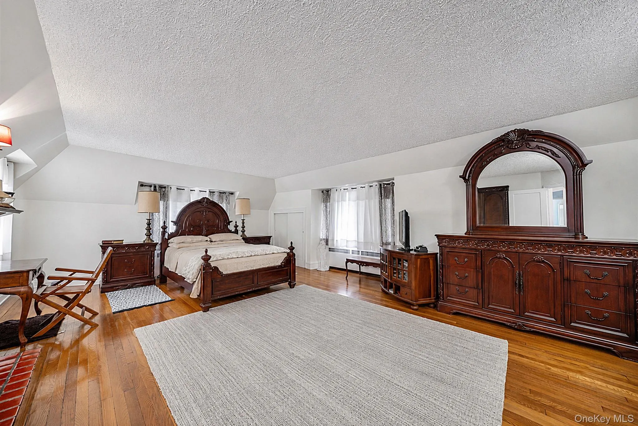 Spacious room featuring wood-finish flooring, white walls, and a sloped ceiling Spacious room featuring wood-finish flooring, white walls, and a sloped ceiling