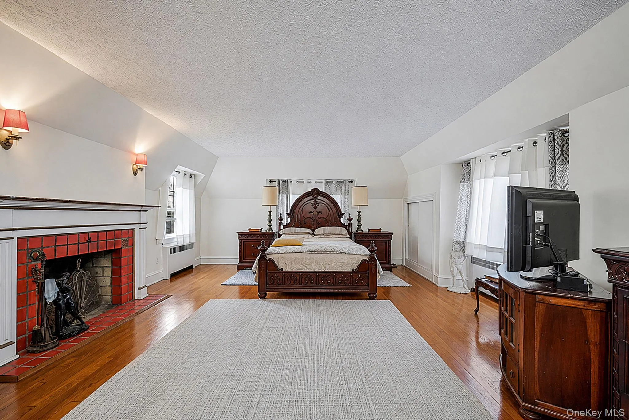 Room featuring polished wood flooring, a decorative fireplace with red tile surround, and multiple windows Room featuring polished wood flooring, a decorative fireplace with red tile surround, and multiple windows