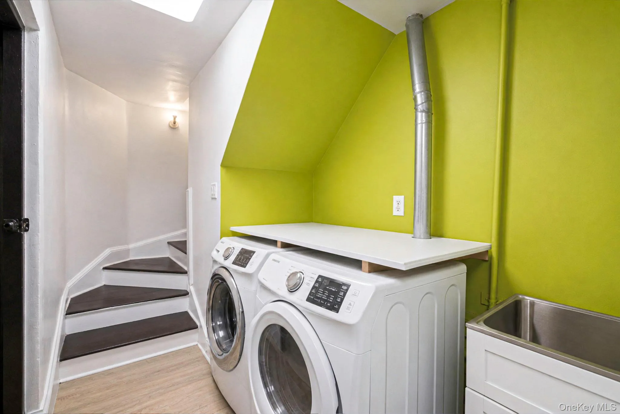 Dedicated laundry area featuring a front-loading washer and dryer, a utility sink with a white base cabinet, a built-in countertop, and a skylight Dedicated laundry area featuring a front-loading washer and dryer, a utility sink with a white base cabinet, a built-in countertop, and a skylight