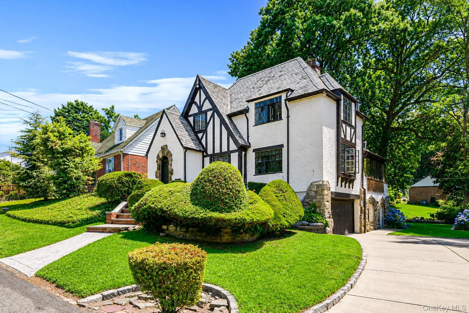 Tudor-style residence featuring a prominent front gable, stucco and half-timbering accents, a stone-clad foundation, and a slate-tile roof Tudor-style residence featuring a prominent front gable, stucco and half-timbering accents, a stone-clad foundation, and a slate-tile roof