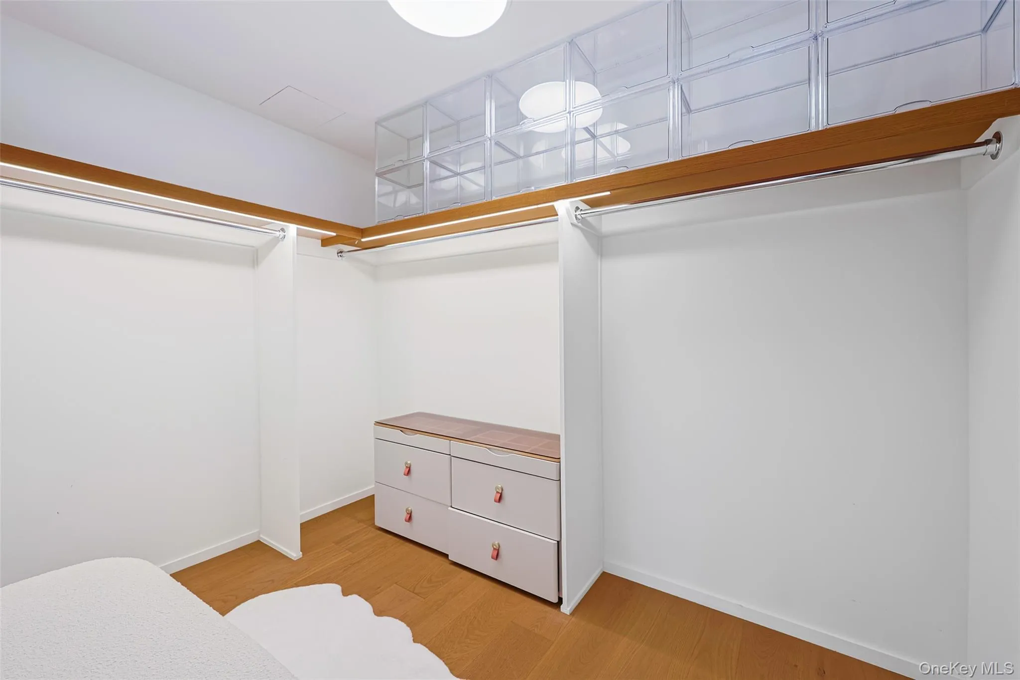 Primary Bedroom Walk-in closet featuring wood-finish flooring, white walls, built-in clothing rods, integrated overhead lighting. Primary Bedroom Walk-in closet featuring wood-finish flooring, white walls, built-in clothing rods, integrated overhead lighting.