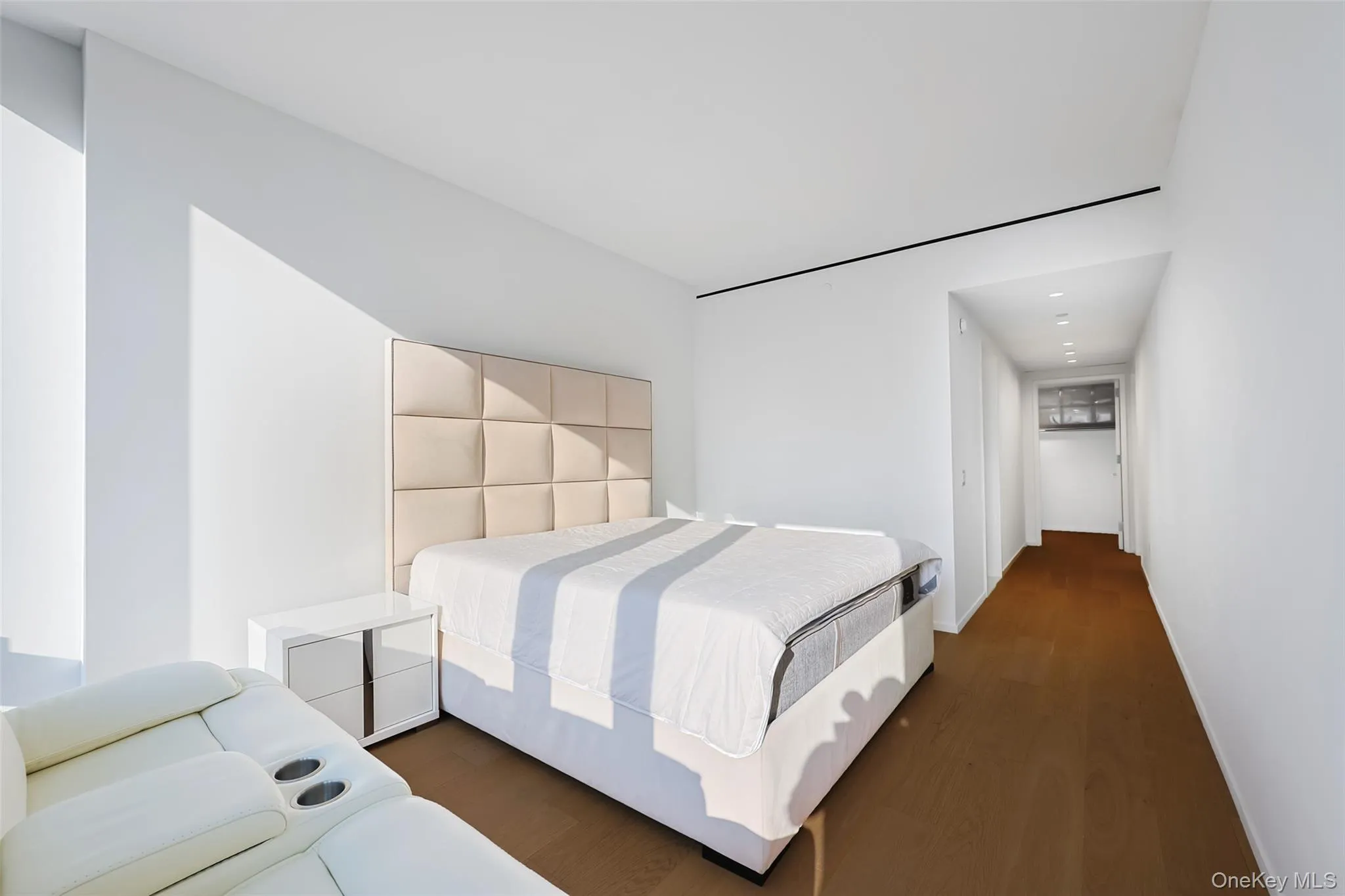 Bedroom featuring an upholstered headboard, white walls, wood-finish flooring, recessed lighting, and a linear ceiling light fixture Bedroom featuring an upholstered headboard, white walls, wood-finish flooring, recessed lighting, and a linear ceiling light fixture