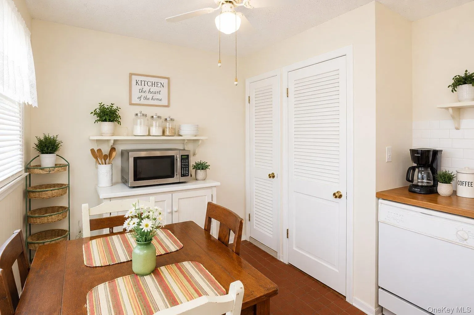 Compact kitchen space featuring a wood-finish dining table, white built-in cabinetry, and white louvered closet doors Compact kitchen space featuring a wood-finish dining table, white built-in cabinetry, and white louvered closet doors