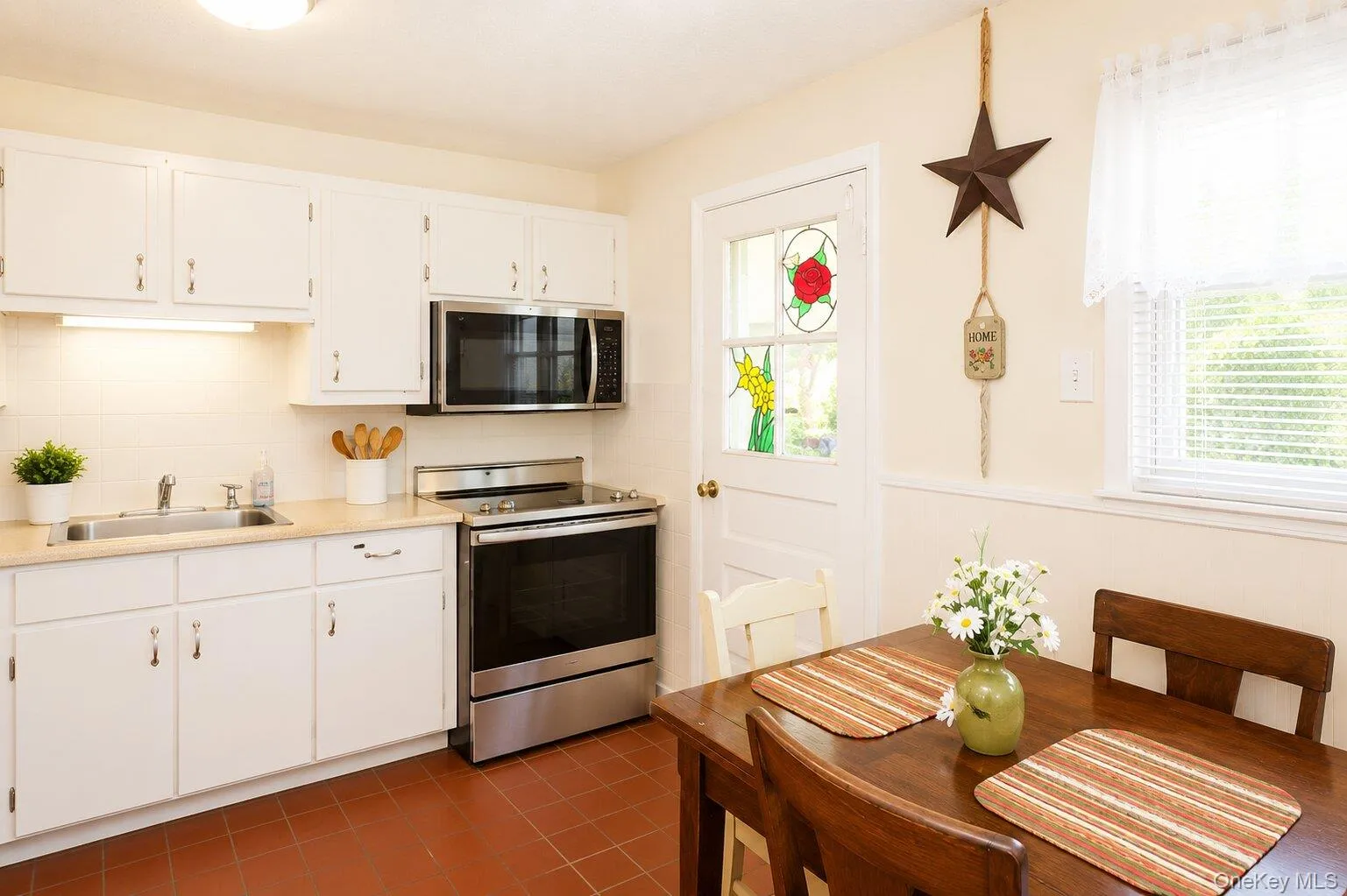 Eat-in kitchen featuring white cabinetry, stainless steel appliances, a tile backsplash, light-toned countertops, and wood-finish flooring Eat-in kitchen featuring white cabinetry, stainless steel appliances, a tile backsplash, light-toned countertops, and wood-finish flooring