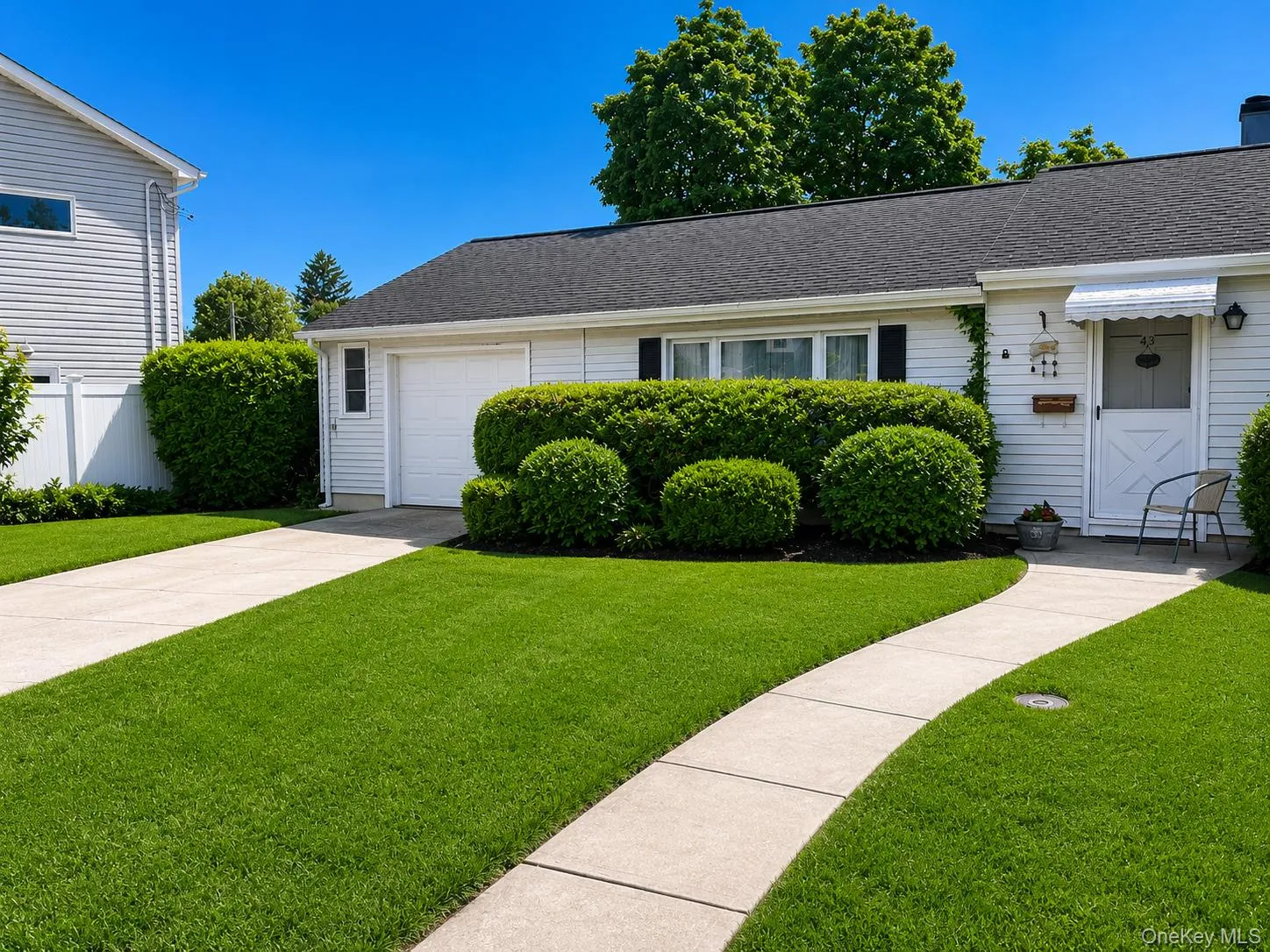 White siding exterior with a dark shingle roof, complemented by a concrete driveway and walkway White siding exterior with a dark shingle roof, complemented by a concrete driveway and walkway