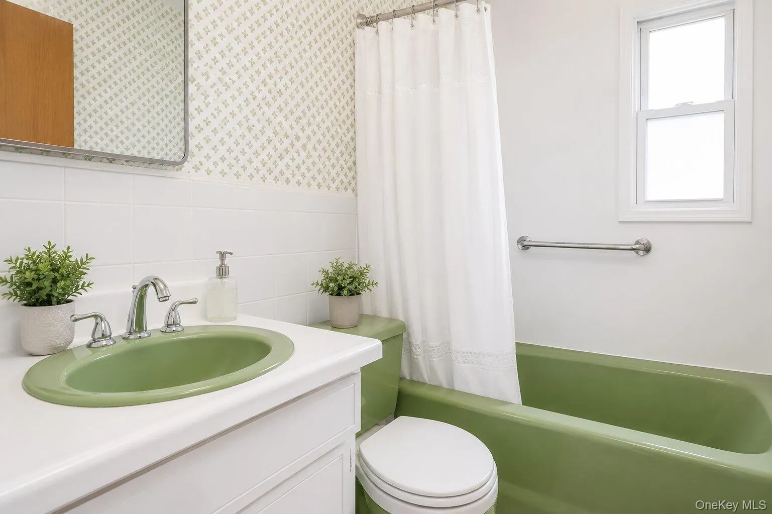 Bathroom featuring a green drop-in sink, white vanity, white tile wainscoting, green bathtub, and a window providing natural light Bathroom featuring a green drop-in sink, white vanity, white tile wainscoting, green bathtub, and a window providing natural light